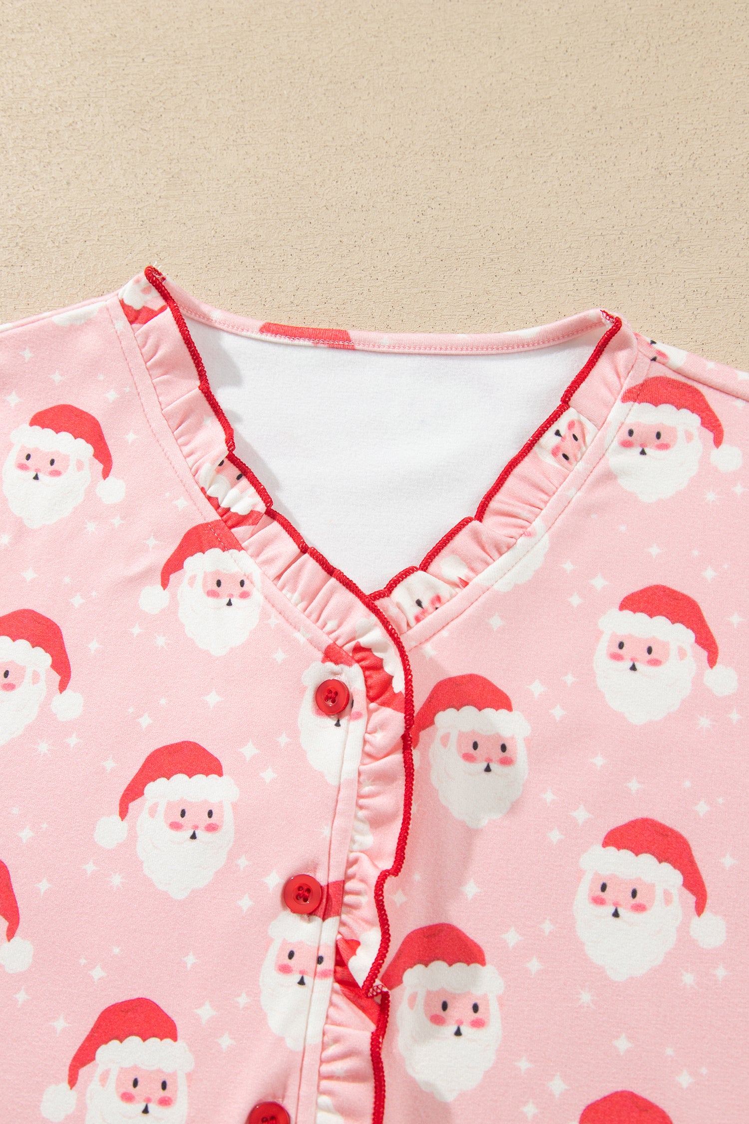 Close-up of red ruffle V neckline and red buttons on pink Santa print pajama top