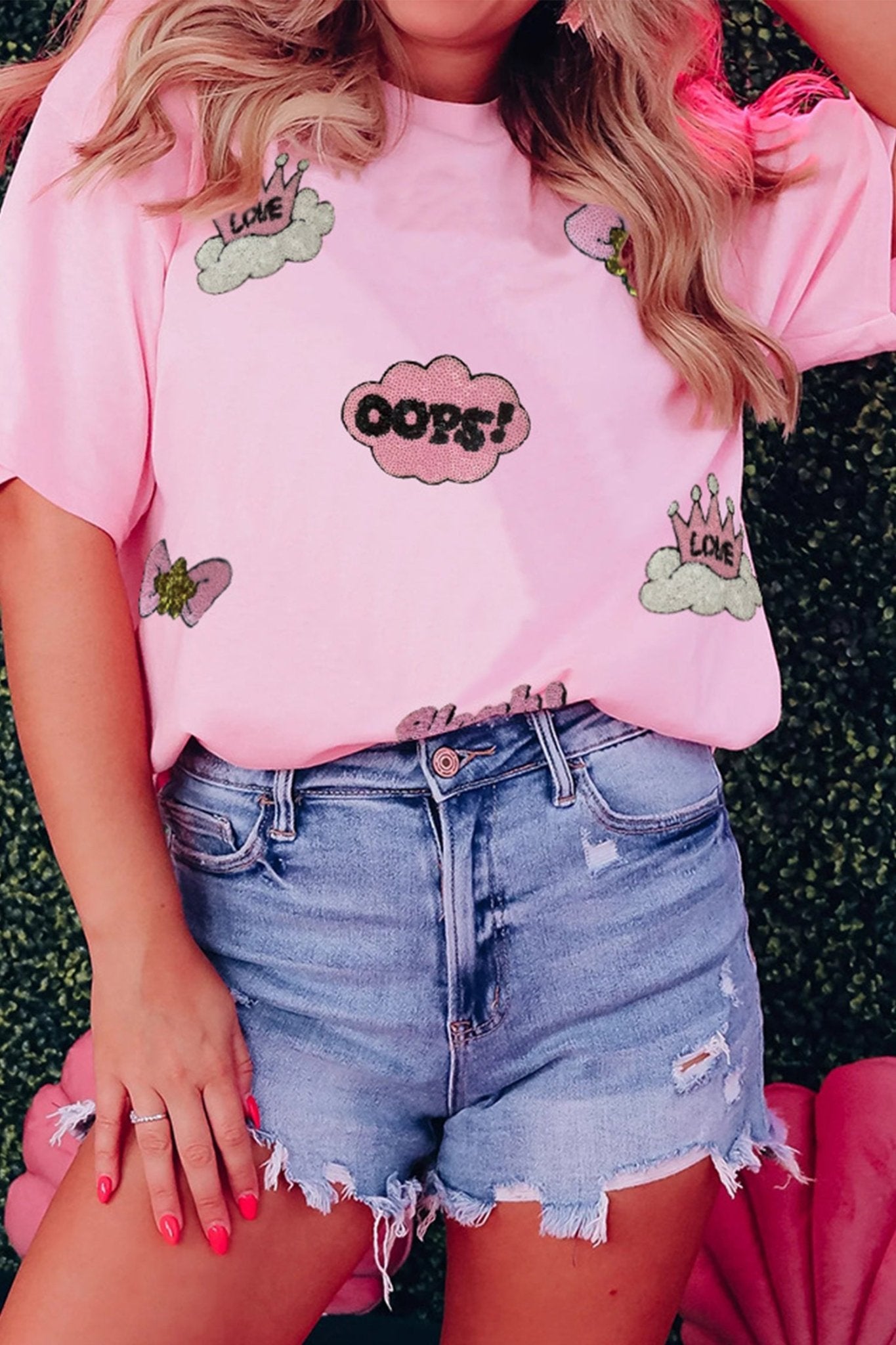 Person wearing a pink t-shirt with cloud and 'OOPS!' design, paired with denim shorts.