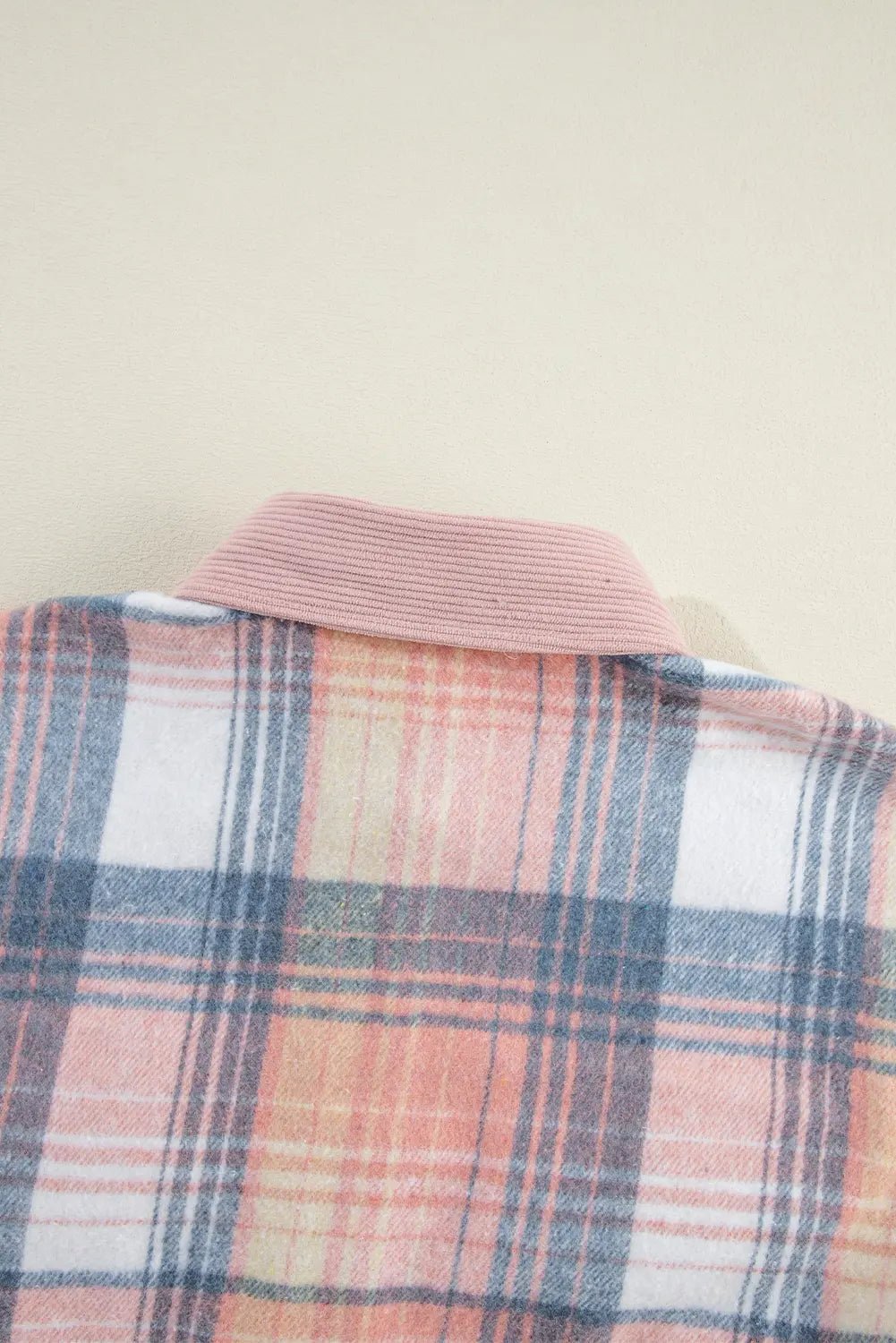 Close-up of a plaid shirt with a pink collar on a beige background