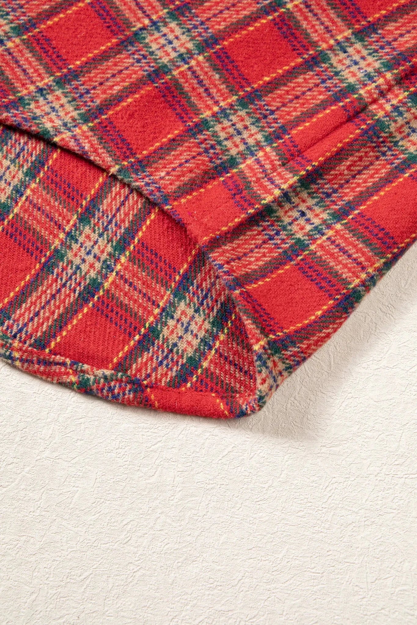 A close-up of a red plaid fabric with green, blue, and beige stripes, folded over on a textured off-white surface.