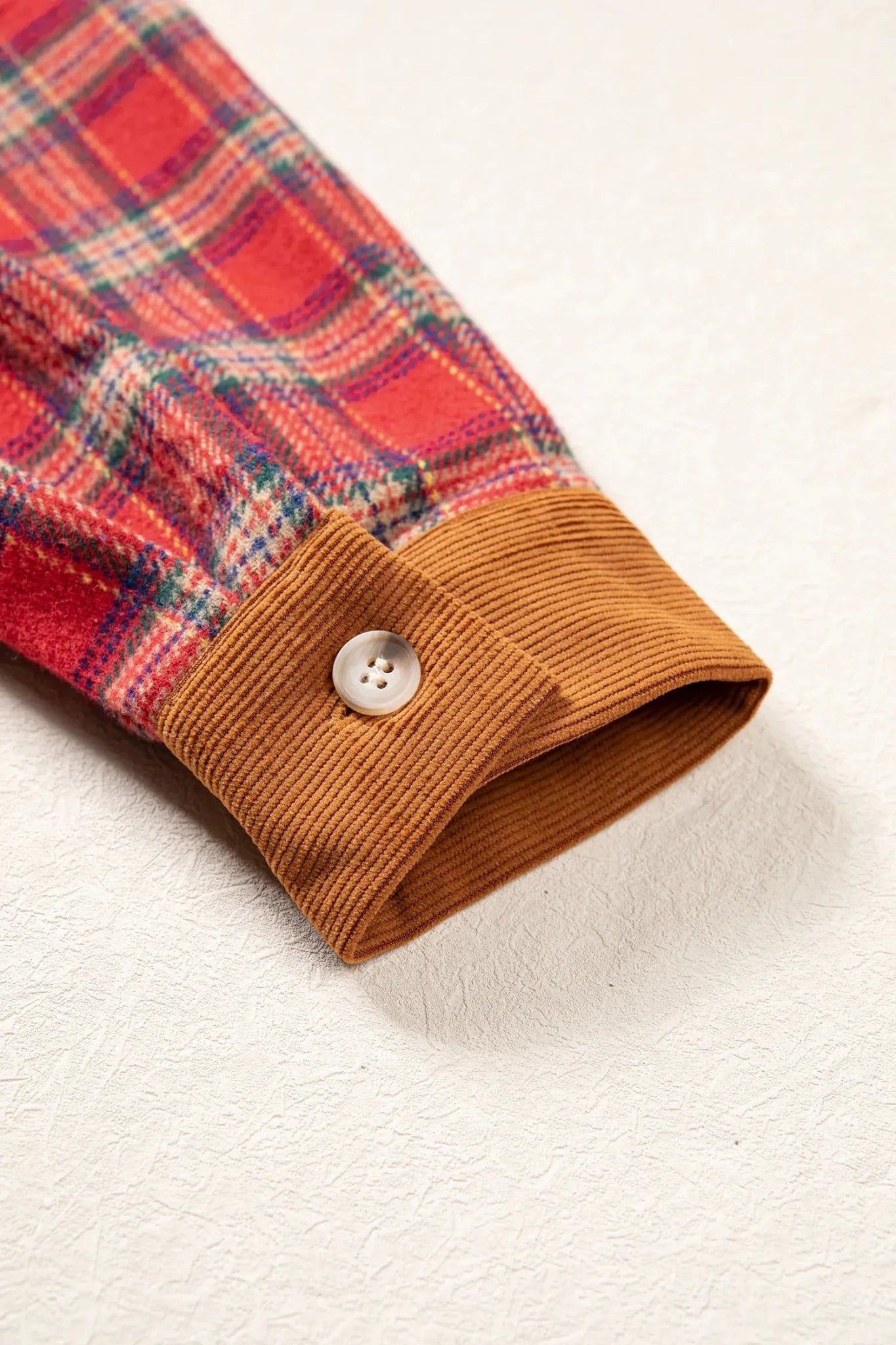 Close-up of plaid shirt sleeve with brown corduroy cuff and white button.