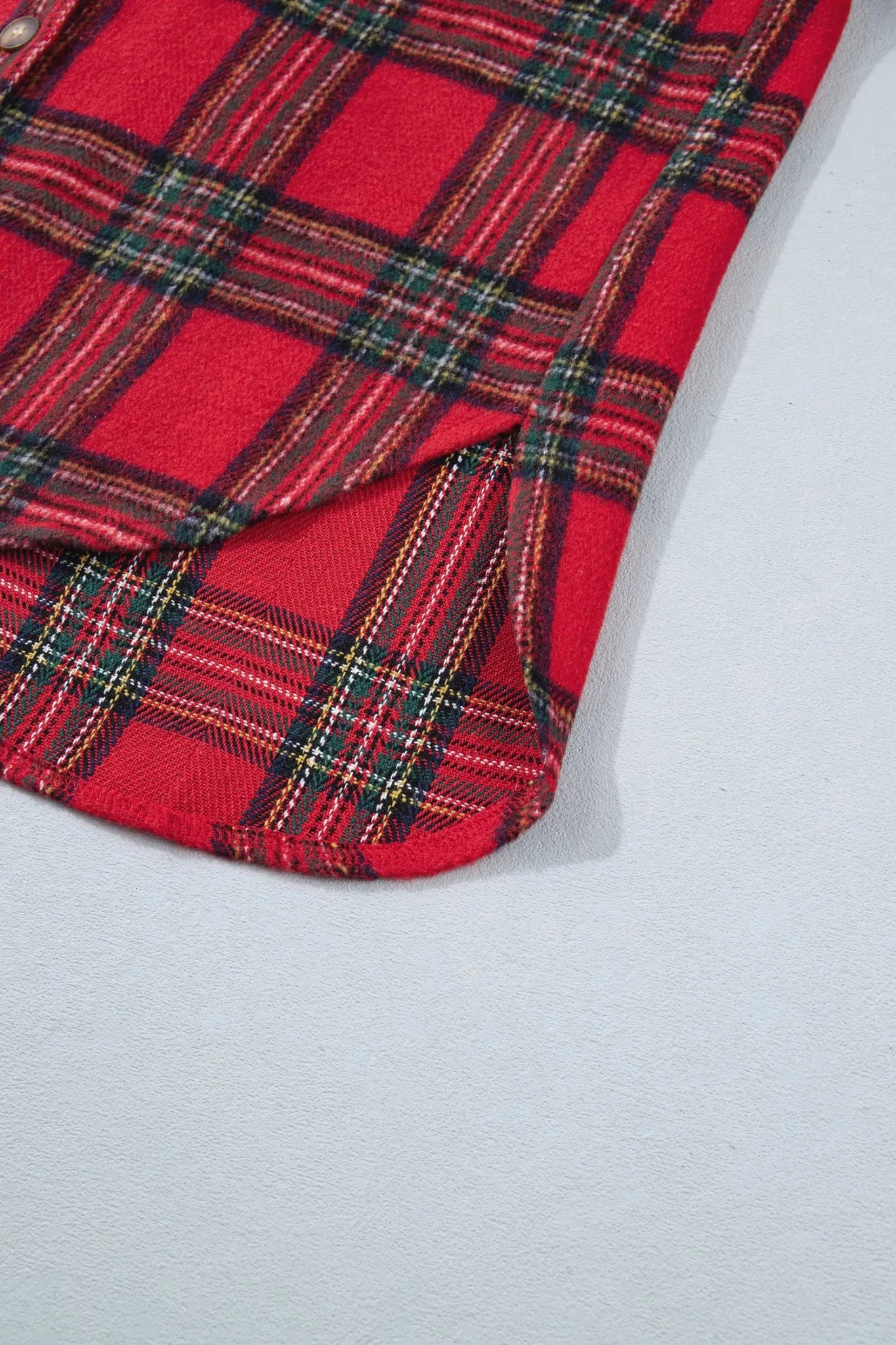 A close-up of a red tartan plaid fabric with black, green, and yellow stripes, folded over on a light gray surface.