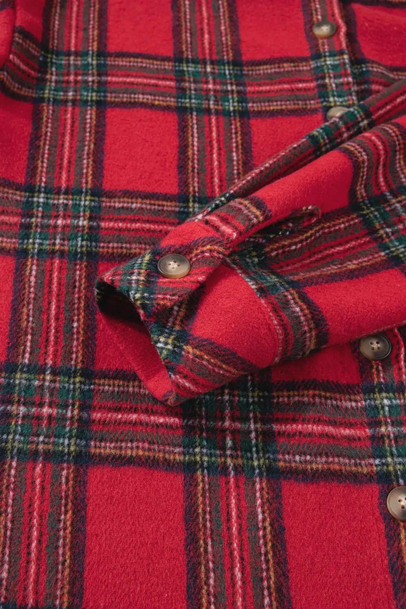 Close-up of a red plaid flannel shirt with green, yellow, and white stripes, featuring a folded cuff with metal snap buttons.