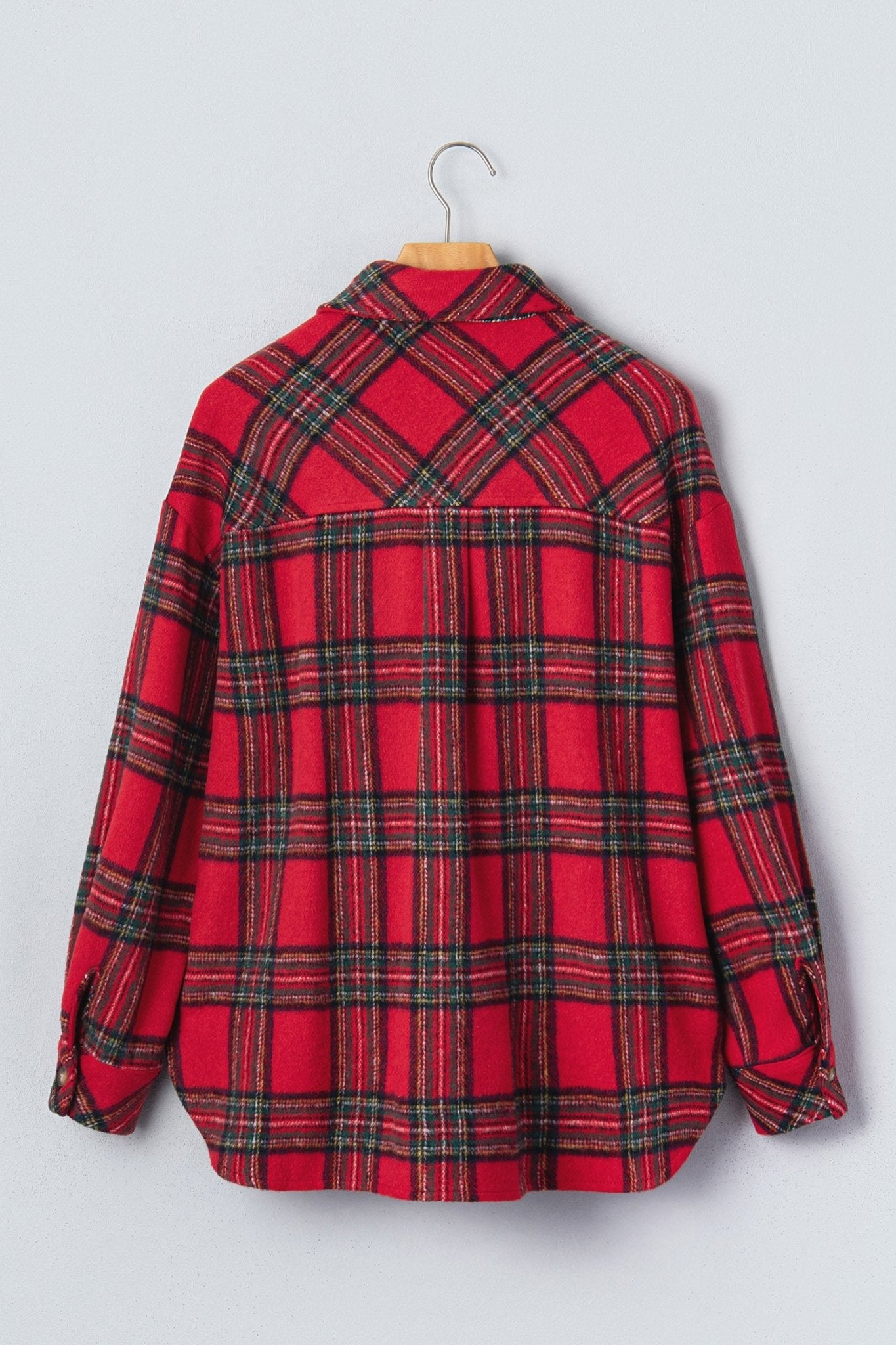 A red plaid long-sleeve button-up shirt hanging on a wooden hanger against a light gray background.