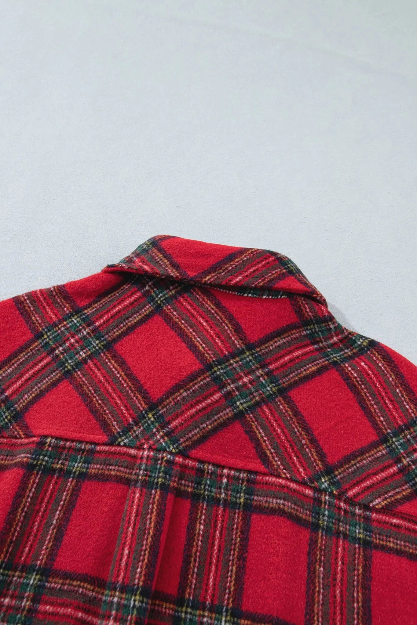 A close-up of a red plaid shirt or jacket fabric, showing the collar and a tartan pattern with black, green, and yellow lines on a light gray background.