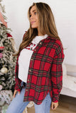 A woman wearing a red and green plaid button-up flannel shirt over a white graphic t-shirt and blue jeans, standing in front of a decorated Christmas tree.