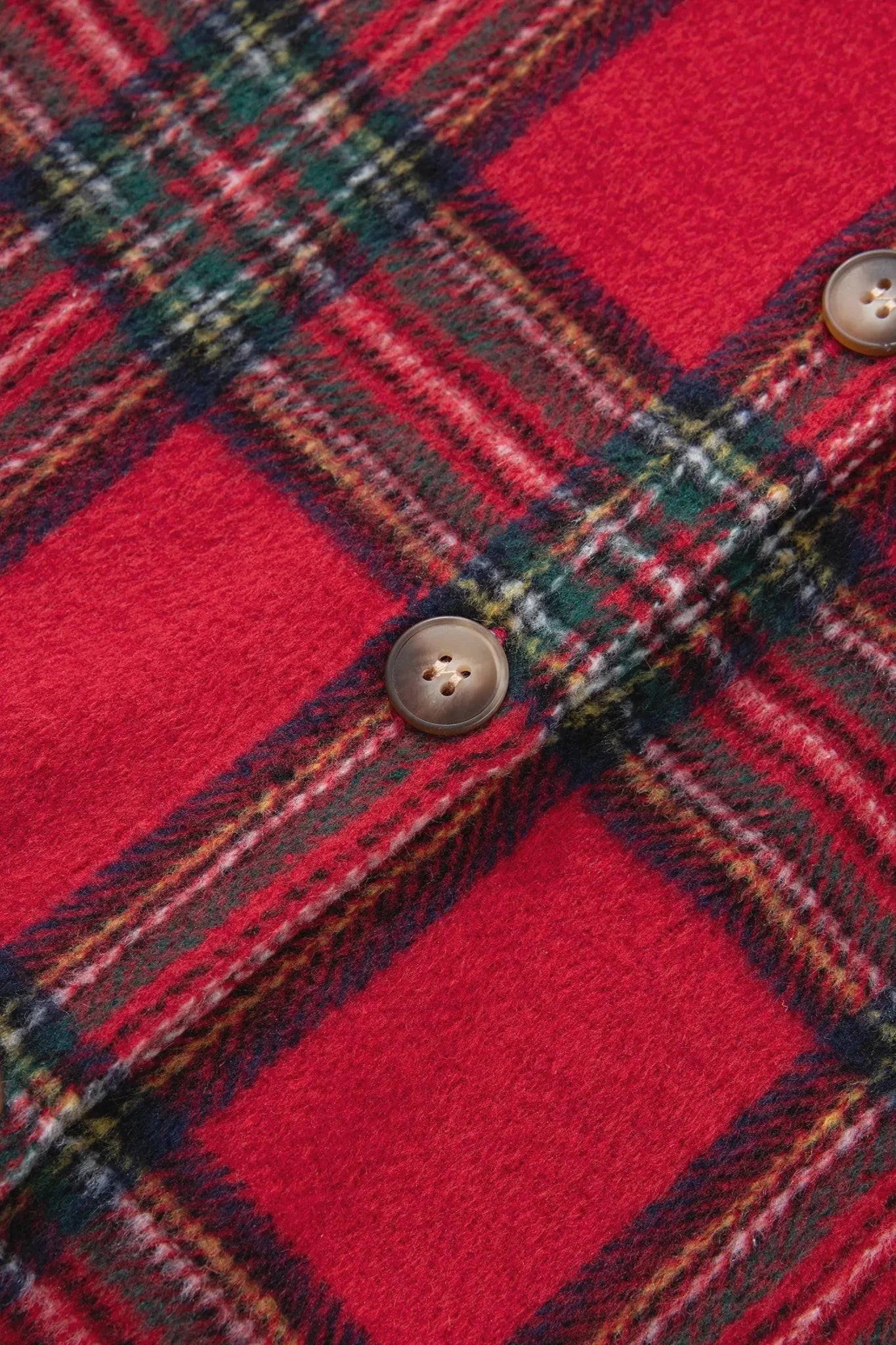 Close-up of a red plaid fabric with green, yellow, and white stripes, featuring two brown buttons.