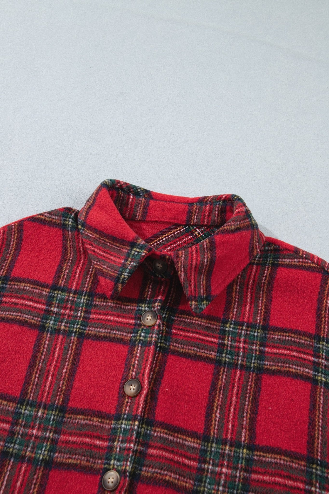 A close-up of a red plaid button-up shirt with a classic collar and brown buttons, laid flat against a light gray background.