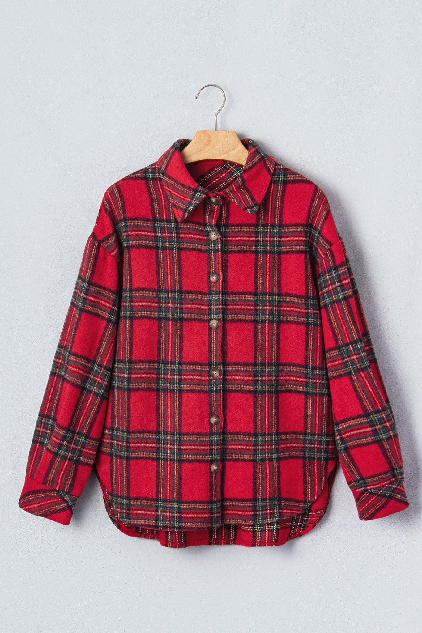 A red plaid button-up shirt with black and green stripes, hanging on a wooden hanger against a light gray background.
