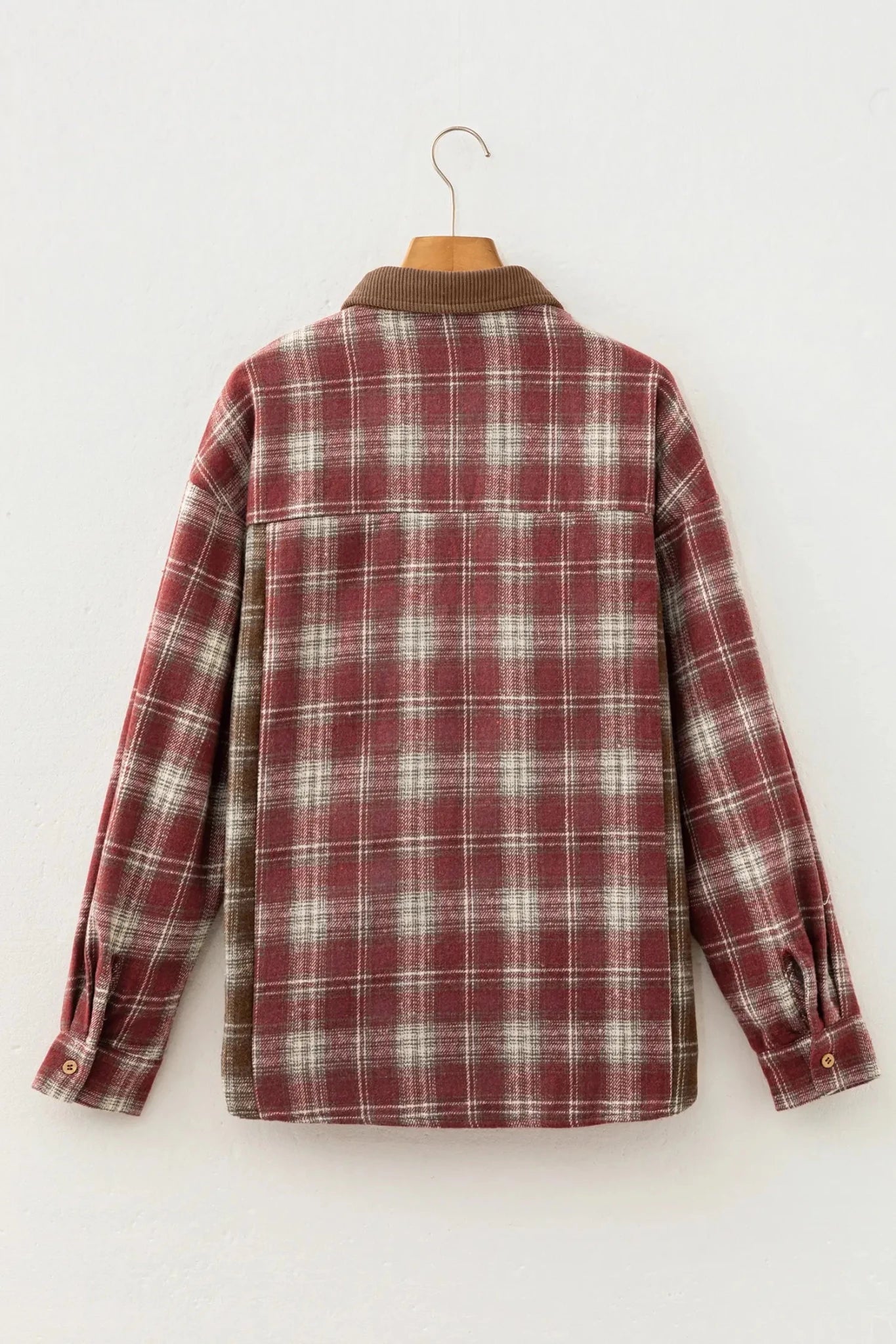 A red and white plaid long-sleeve flannel shirt jacket hanging on a wooden hanger against a plain white wall.
