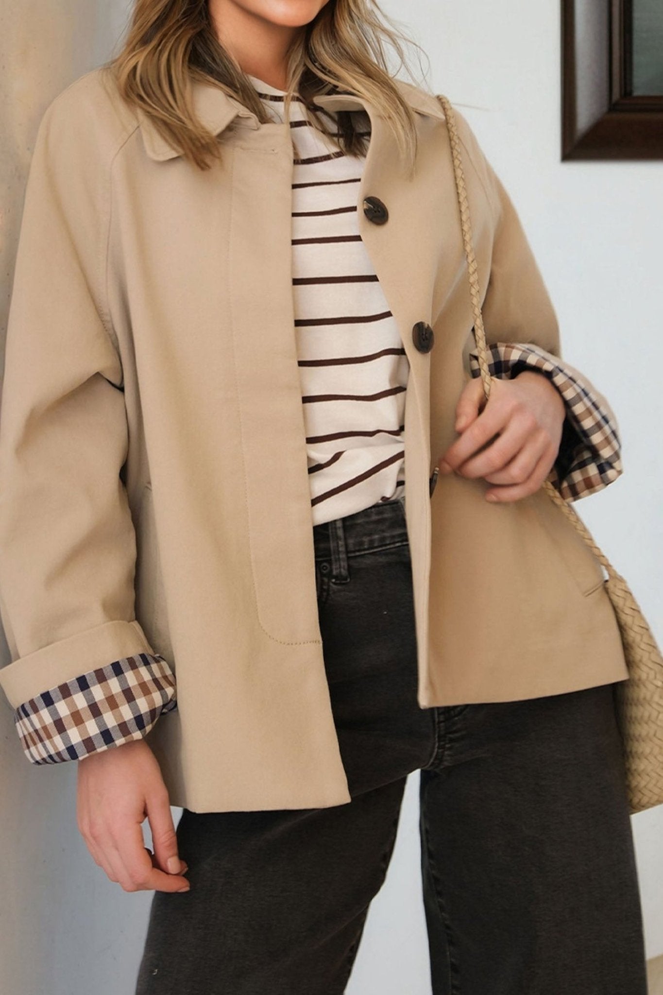 Person wearing a beige coat with plaid cuffs, striped shirt, and dark pants.