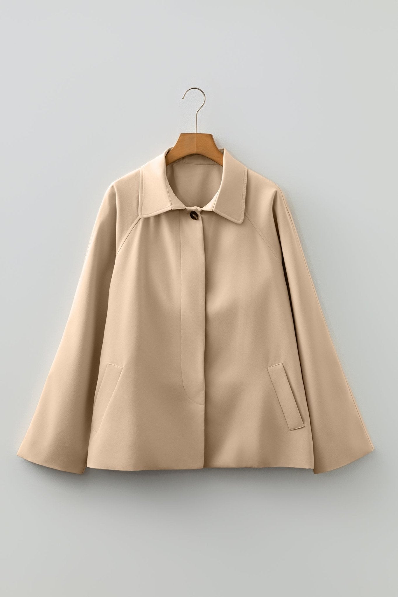 Beige coat on a hanger against a light gray background