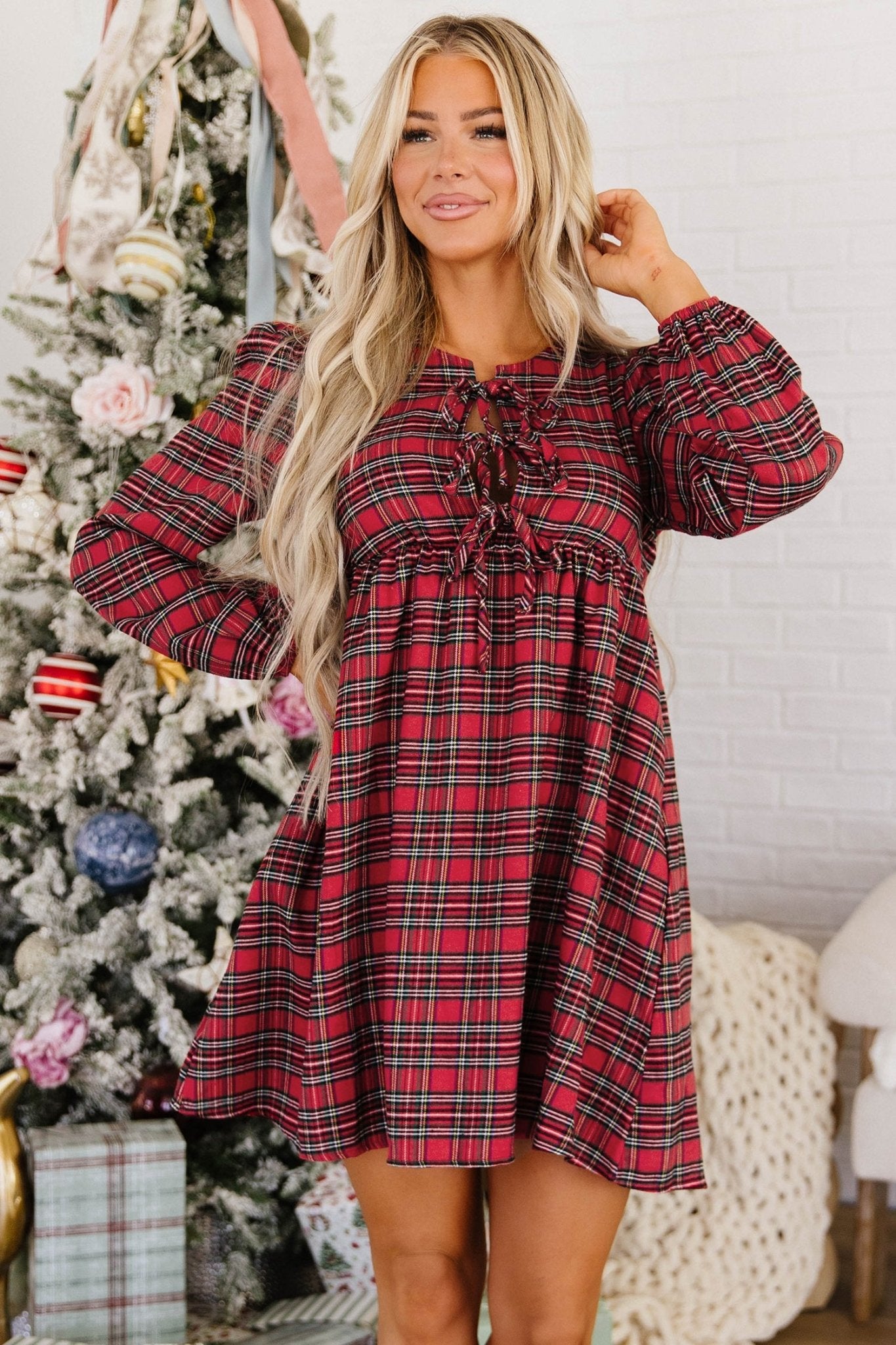 Woman wearing a red and black plaid long-sleeve dress with a tie-neck detail.