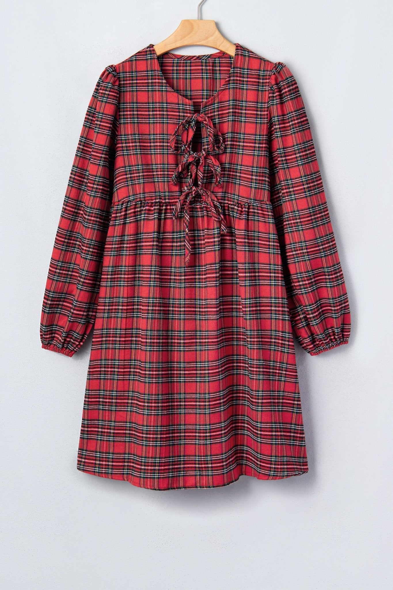 Red and black plaid long-sleeve dress with ruffled tie neckline on a wooden hanger.