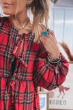 Woman wearing a red plaid long-sleeve dress with tie-front and puff sleeves, layered jewelry.