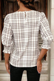 Person wearing a checkered blouse with long sleeves in an indoor setting