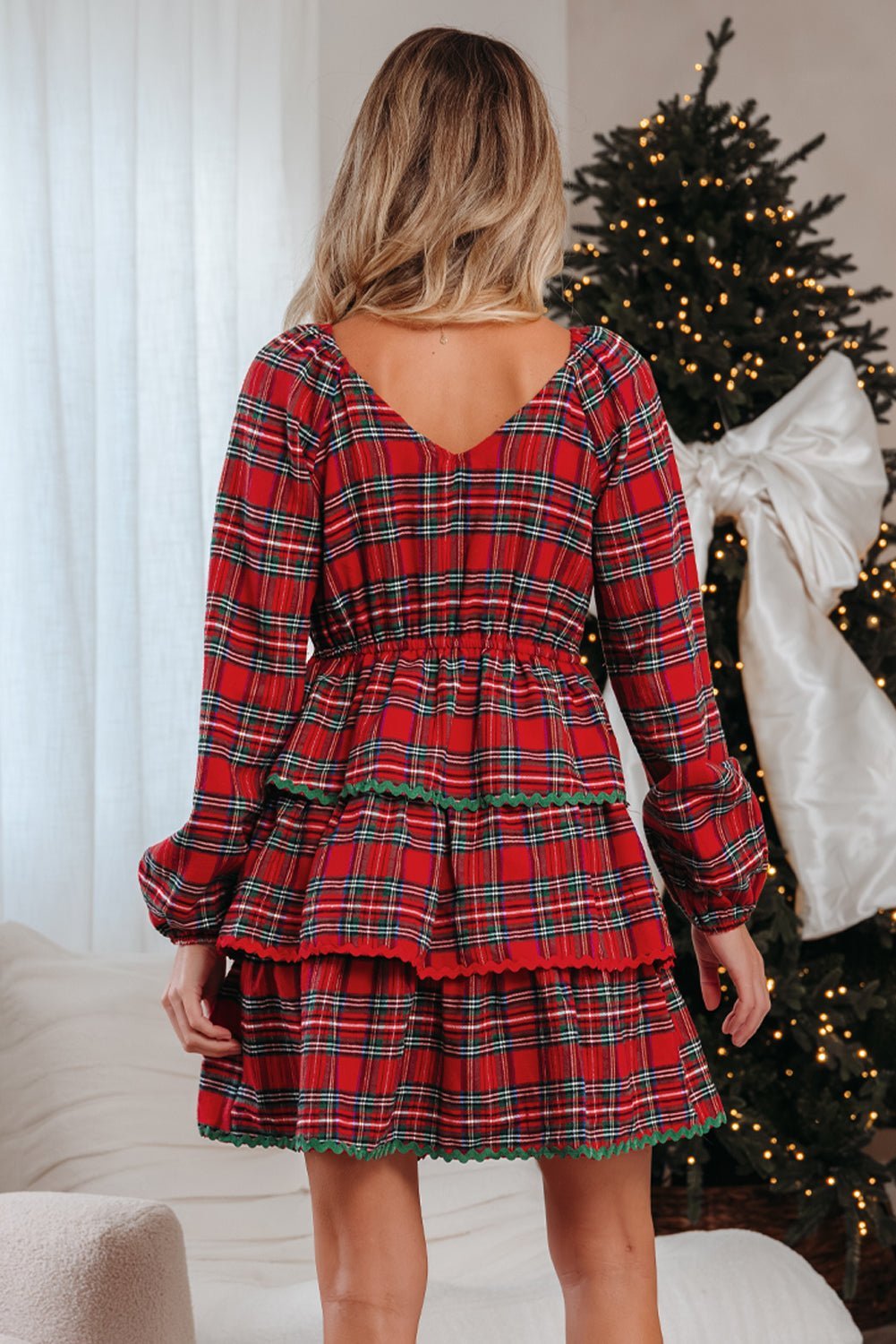 Person wearing a red plaid dress in front of a decorated Christmas tree.