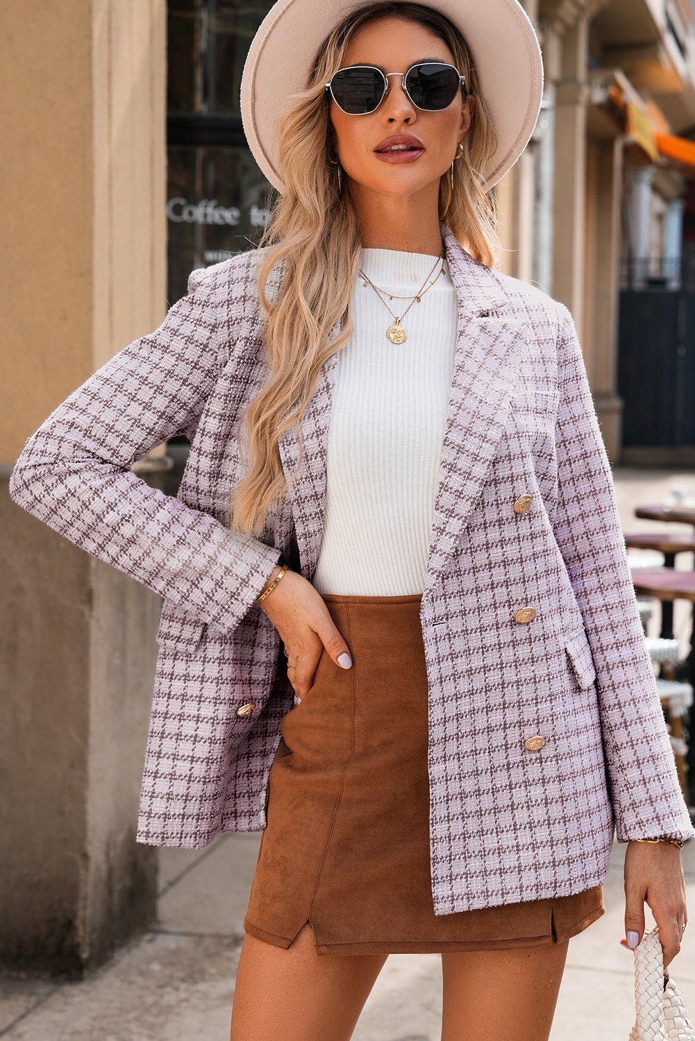 Woman wearing a plaid blazer, white sweater, and brown skirt outdoors.