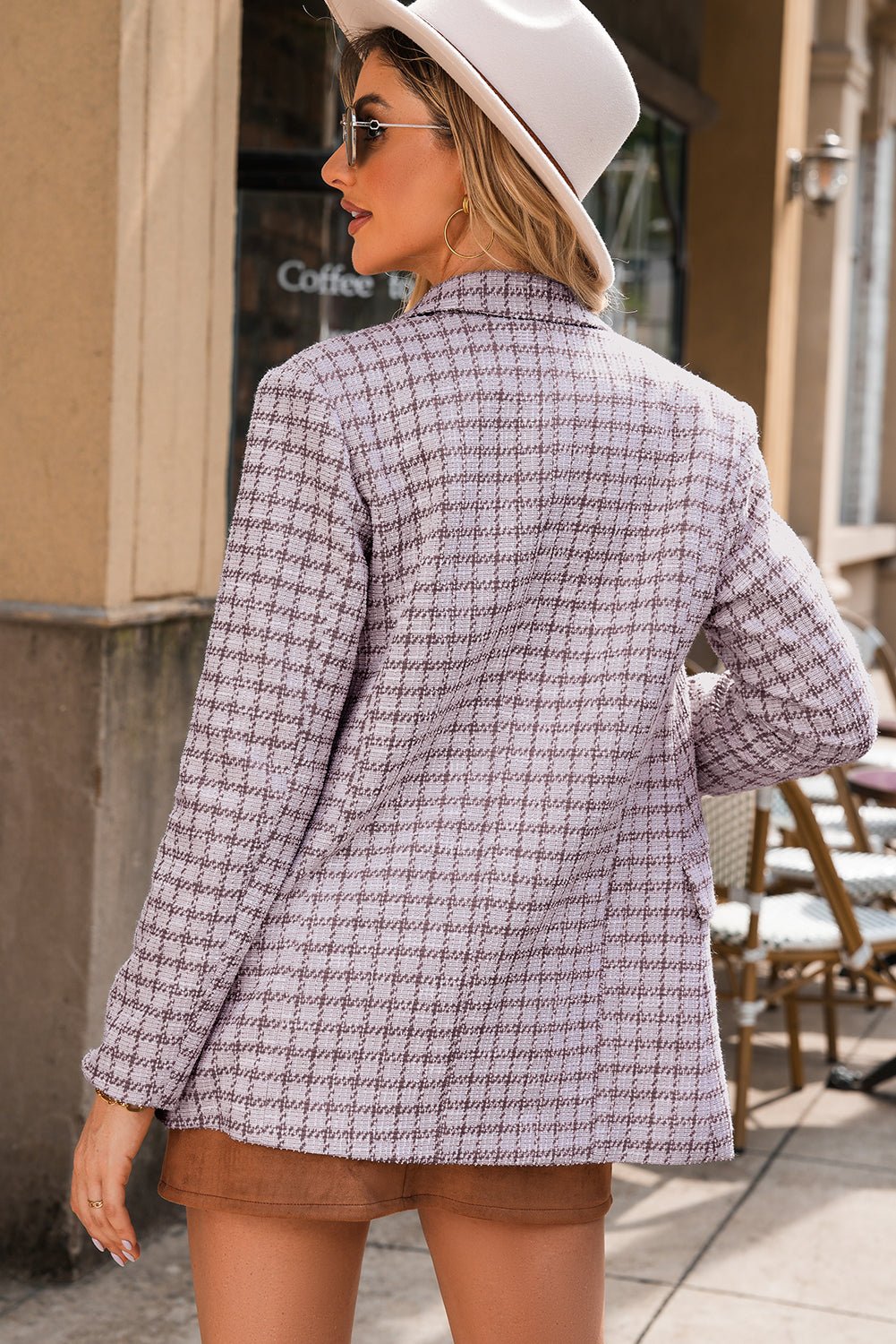 Woman wearing a checkered blazer and white hat outdoors.