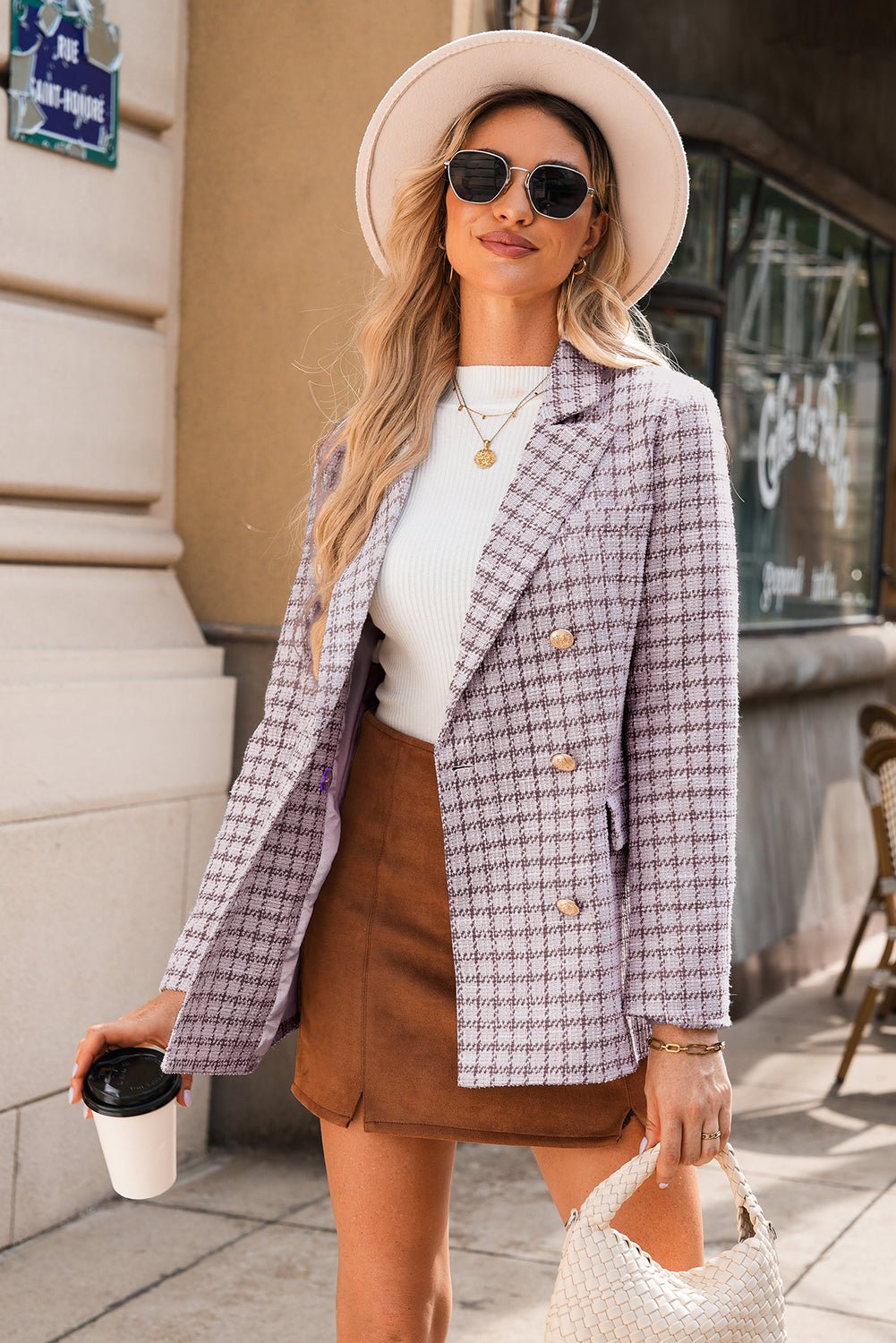 Woman wearing a plaid blazer, white top, and brown skirt on a city street.