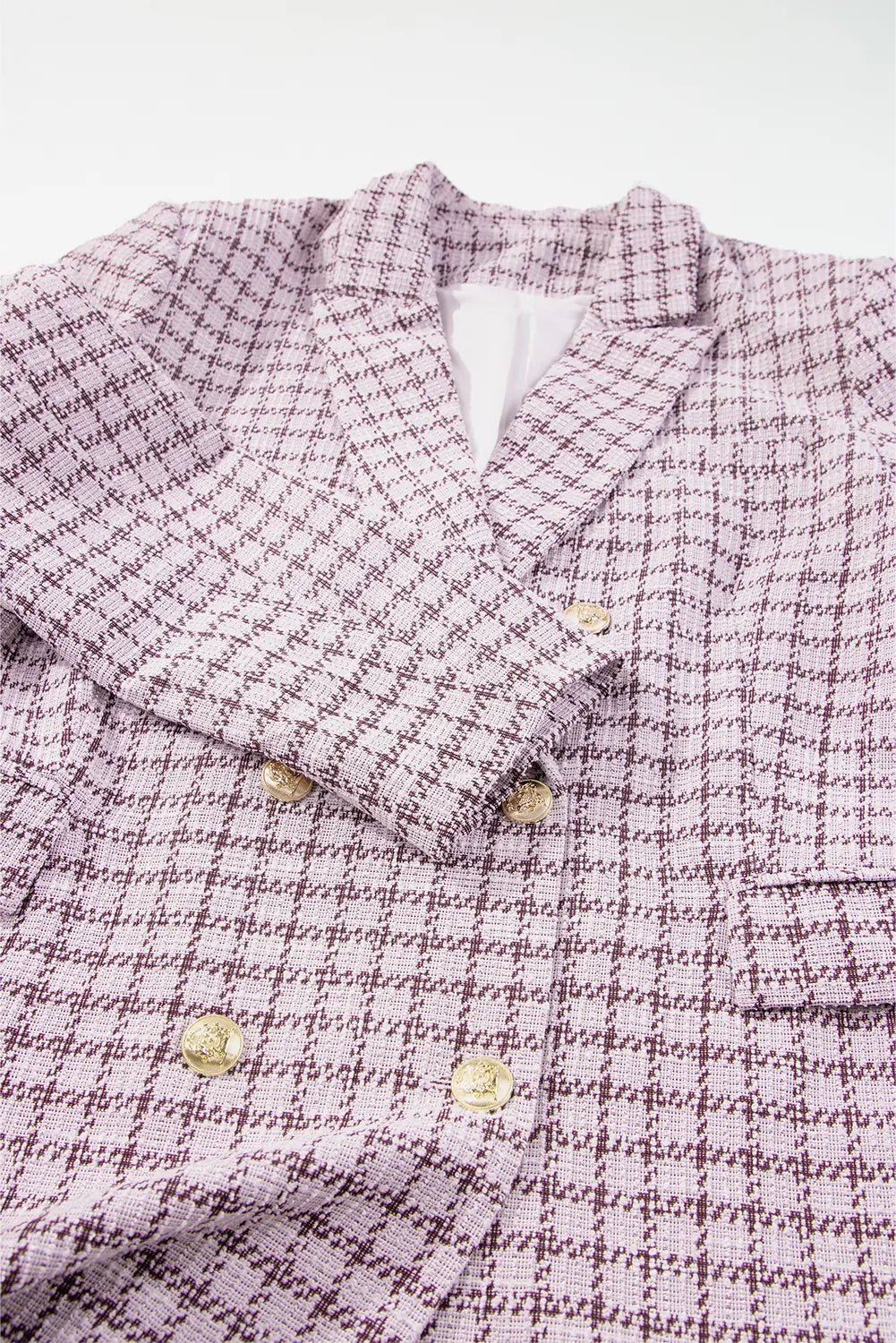 A close-up of a double-breasted blazer in a textured tweed fabric with a purple and white houndstooth pattern, featuring gold buttons.