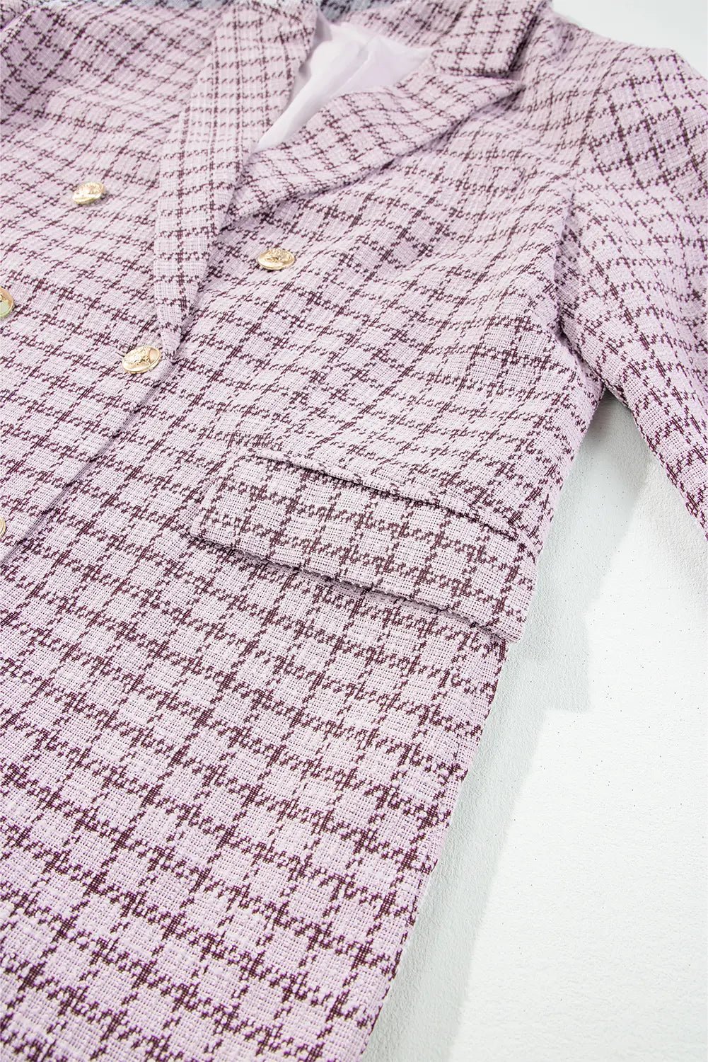 A close-up of a double-breasted blazer in a pink and purple houndstooth pattern, featuring gold buttons and a single-breasted lapel.