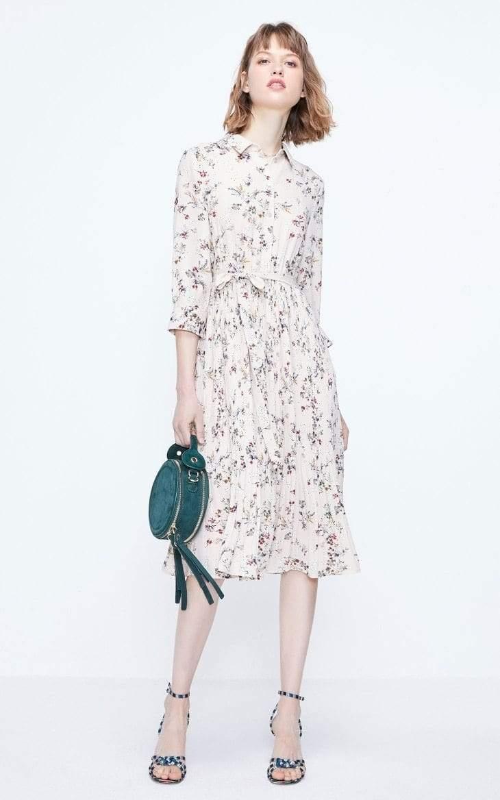 Woman wearing a floral dress holding a green clutch against a white background