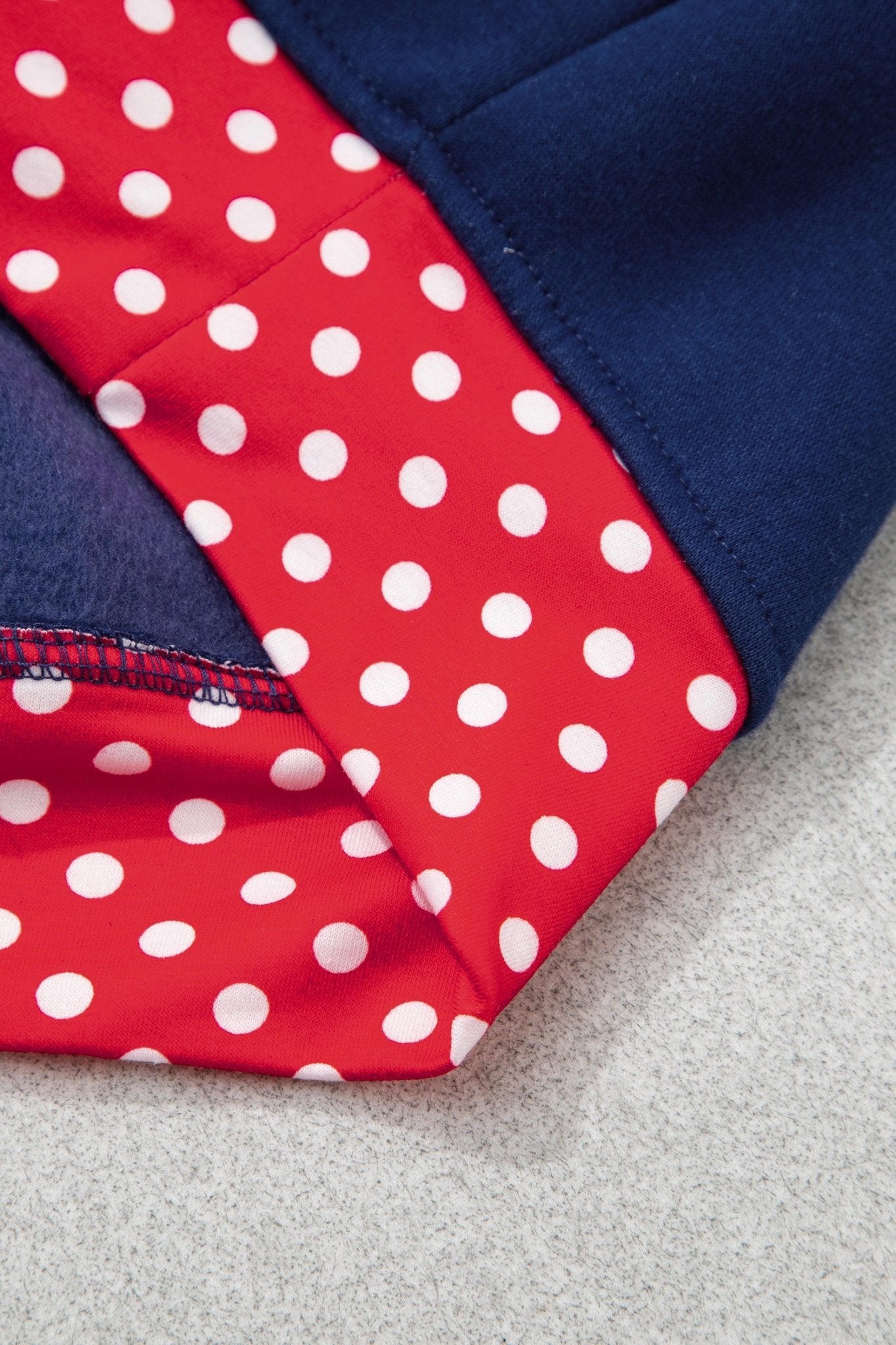 Close-up of navy garment with red fabric panel featuring white polka dots on a light gray surface.