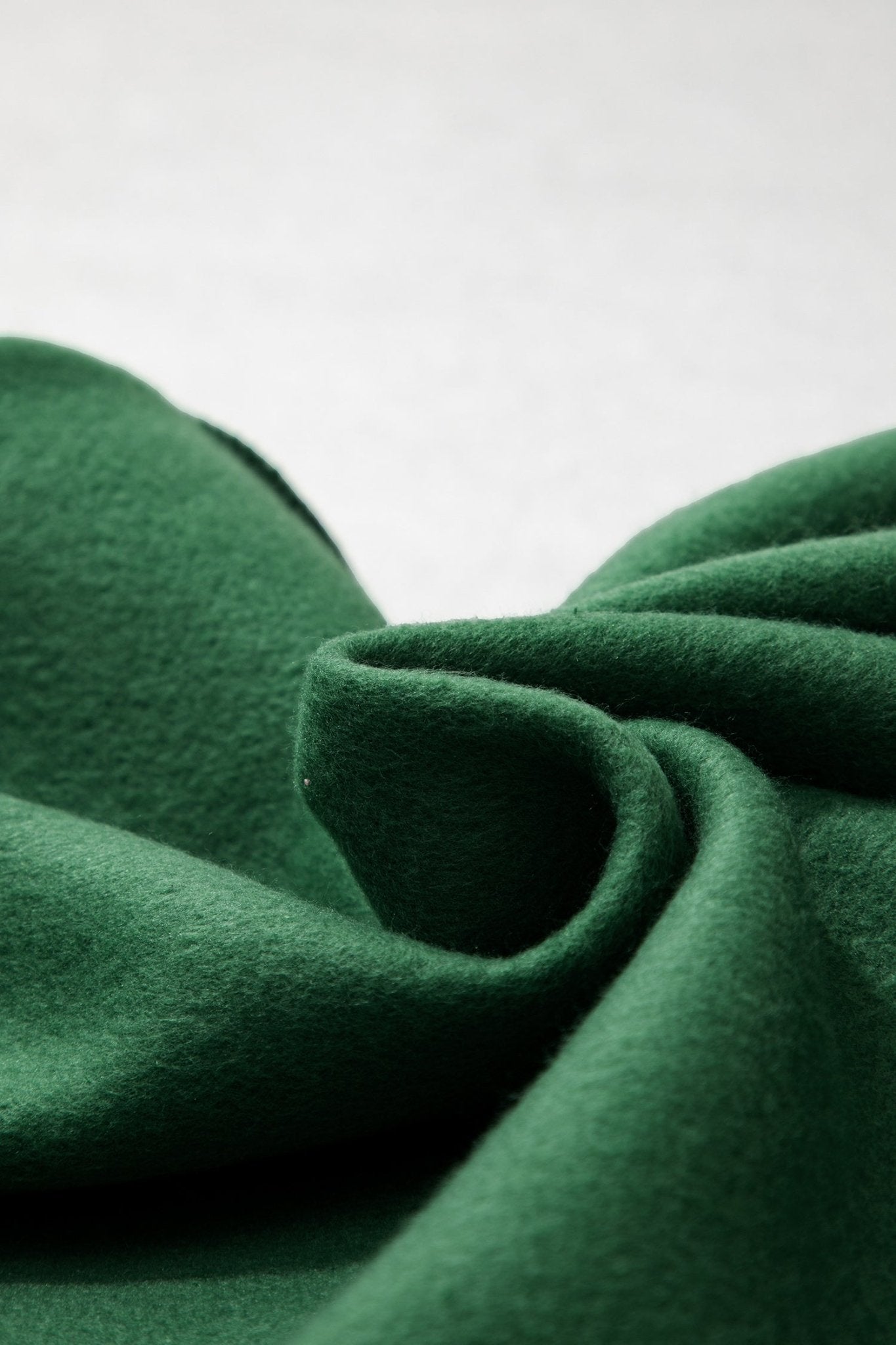 A close-up of dark green fabric with soft folds and a matte texture against a light neutral background.