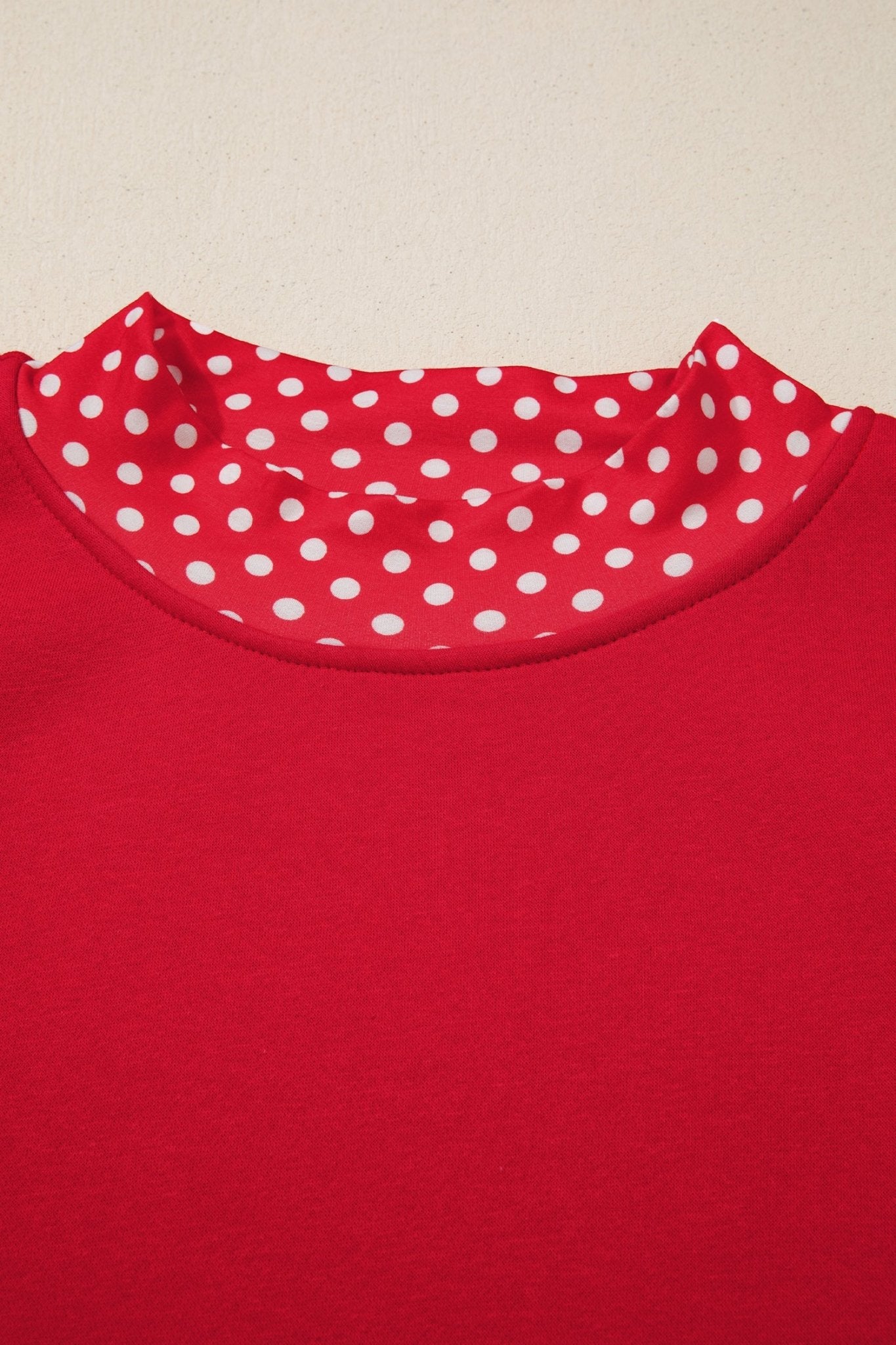 Close-up of red crewneck top with white polka-dot inner collar lining on light beige.