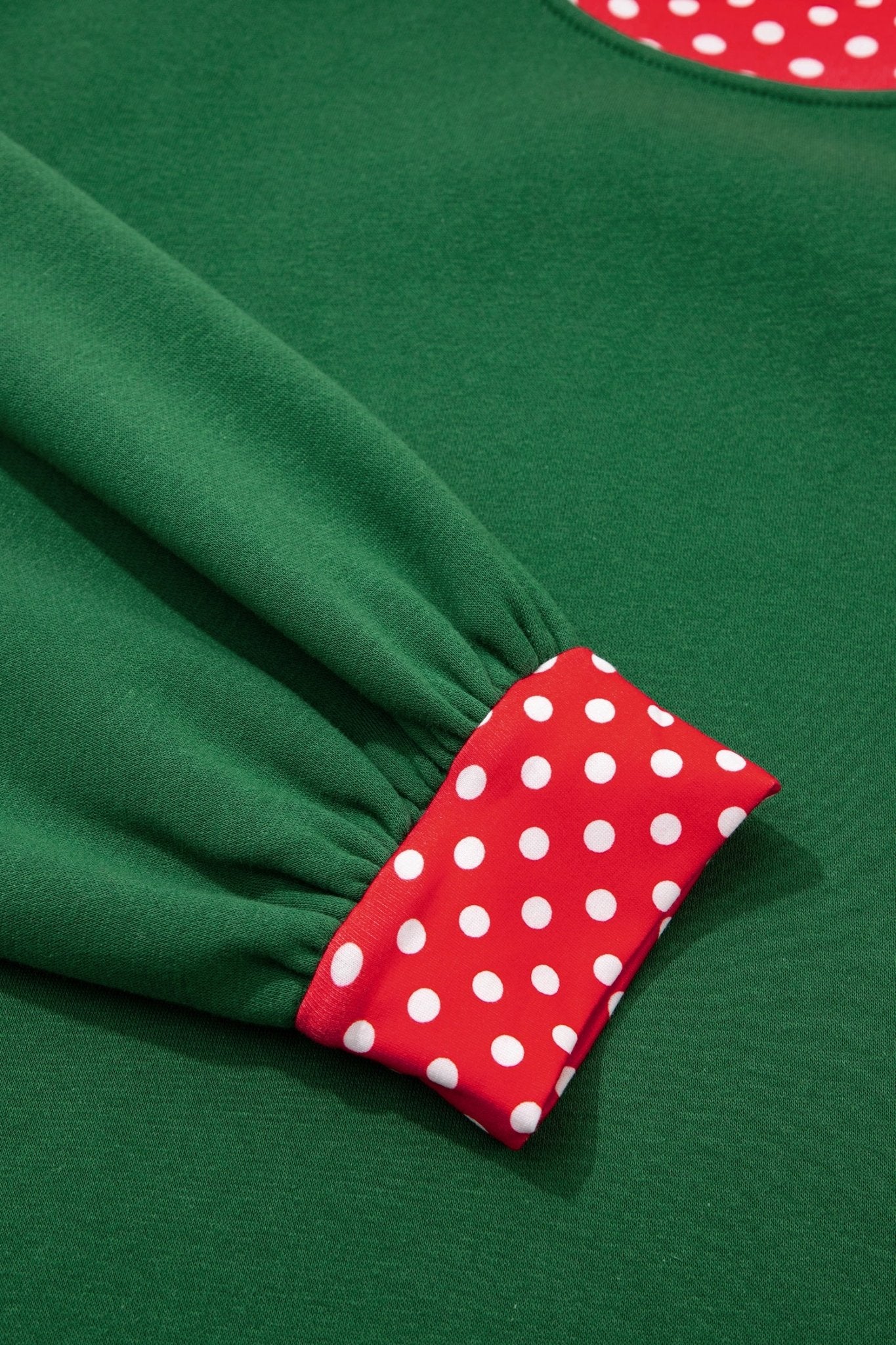 Close-up of green garment with gathered elastic cuff and contrasting red trim featuring white polka dots.