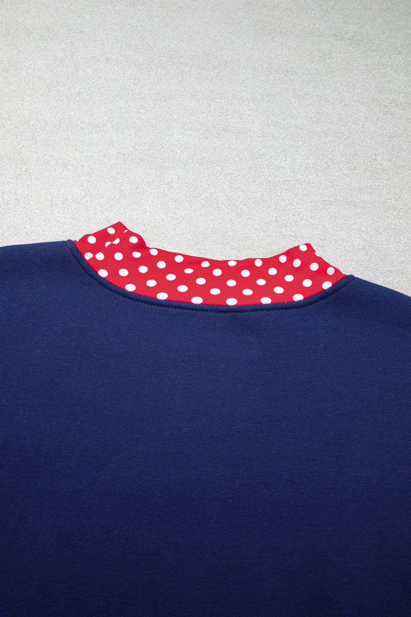 Close-up back view of navy sweatshirt with red collar featuring white polka dots on light gray.