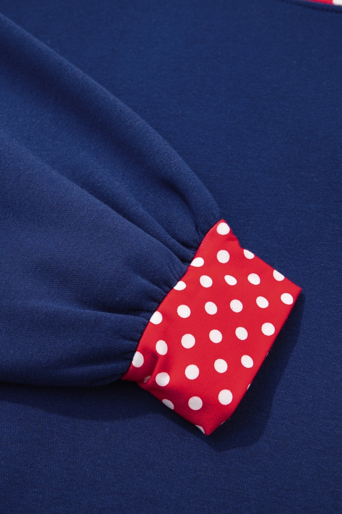 Close-up of navy blue garment sleeve with gathered cuff and red trim featuring white polka dots.