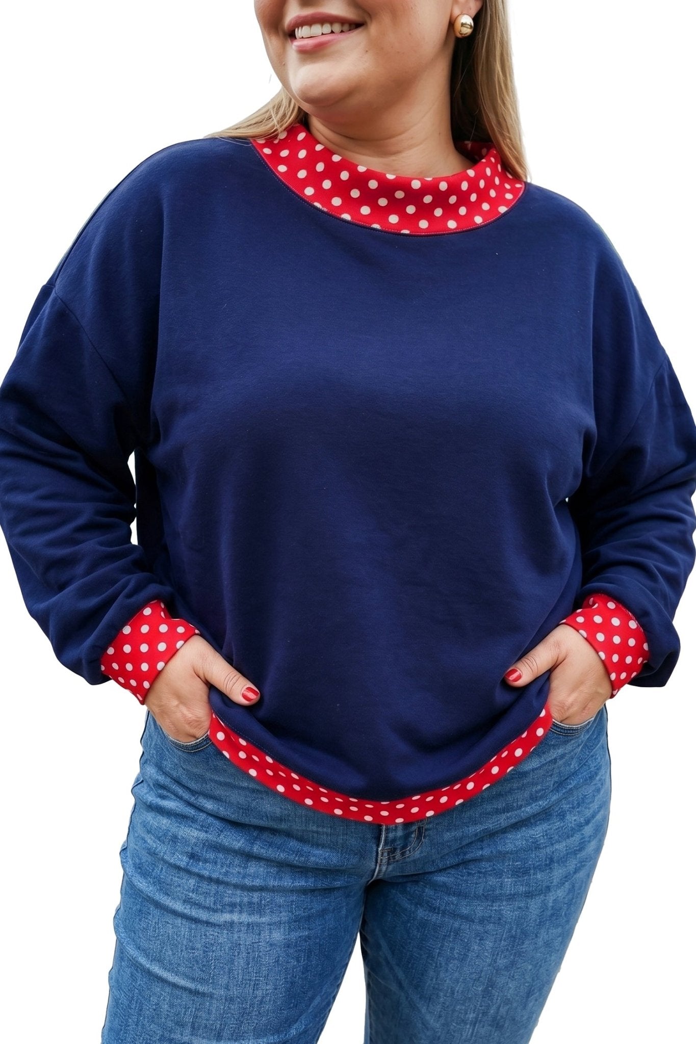 Woman wearing navy blue sweatshirt with red-white polka-dot trim, paired with blue jeans against a white background.