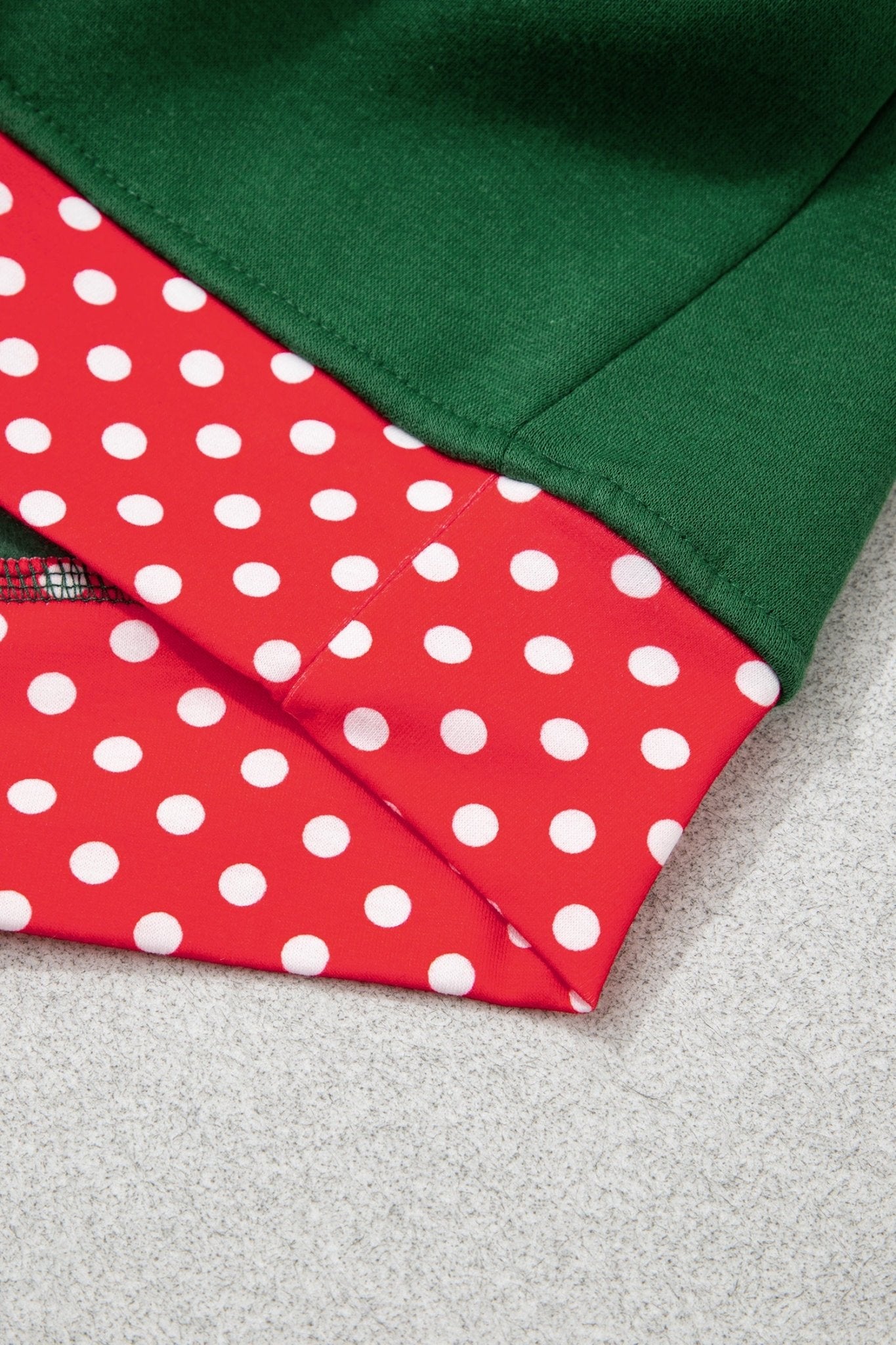 Close-up of folded garment with red-white polka-dot panel and solid dark green fabric on light gray.