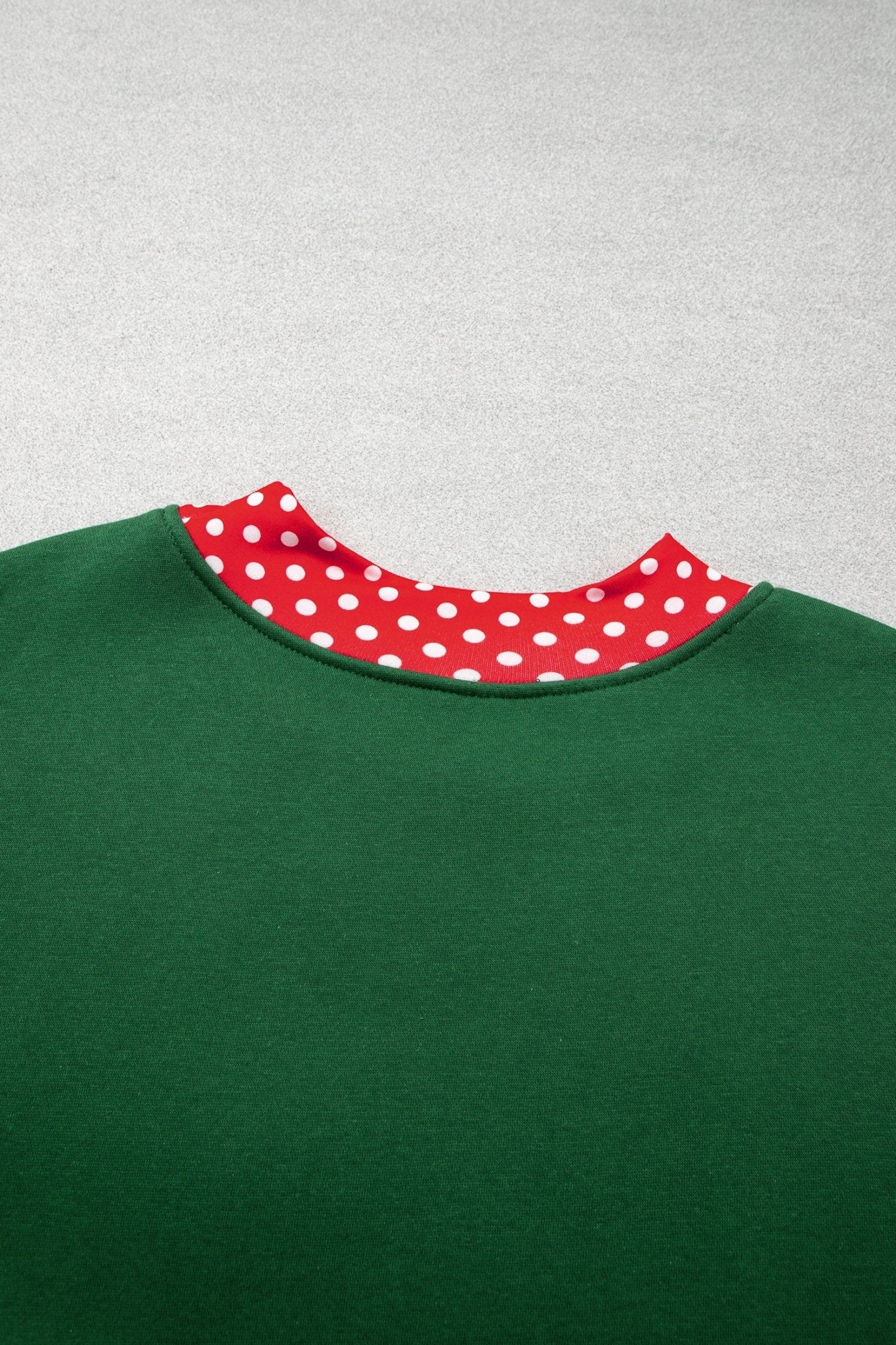 Close-up of green crewneck sweatshirt with red-white polka-dot inner collar lining on light gray.
