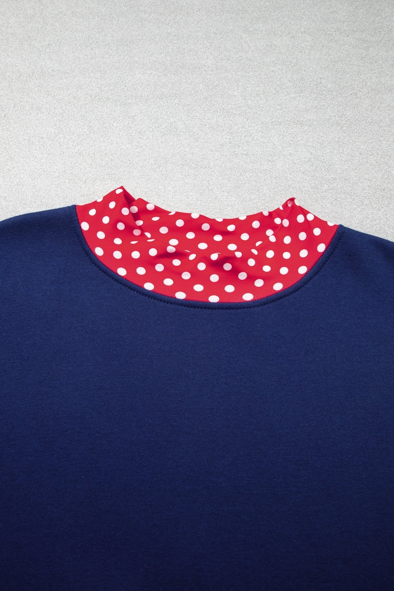 Close-up of navy blue garment with contrasting red collar featuring white polka dots on light gray.