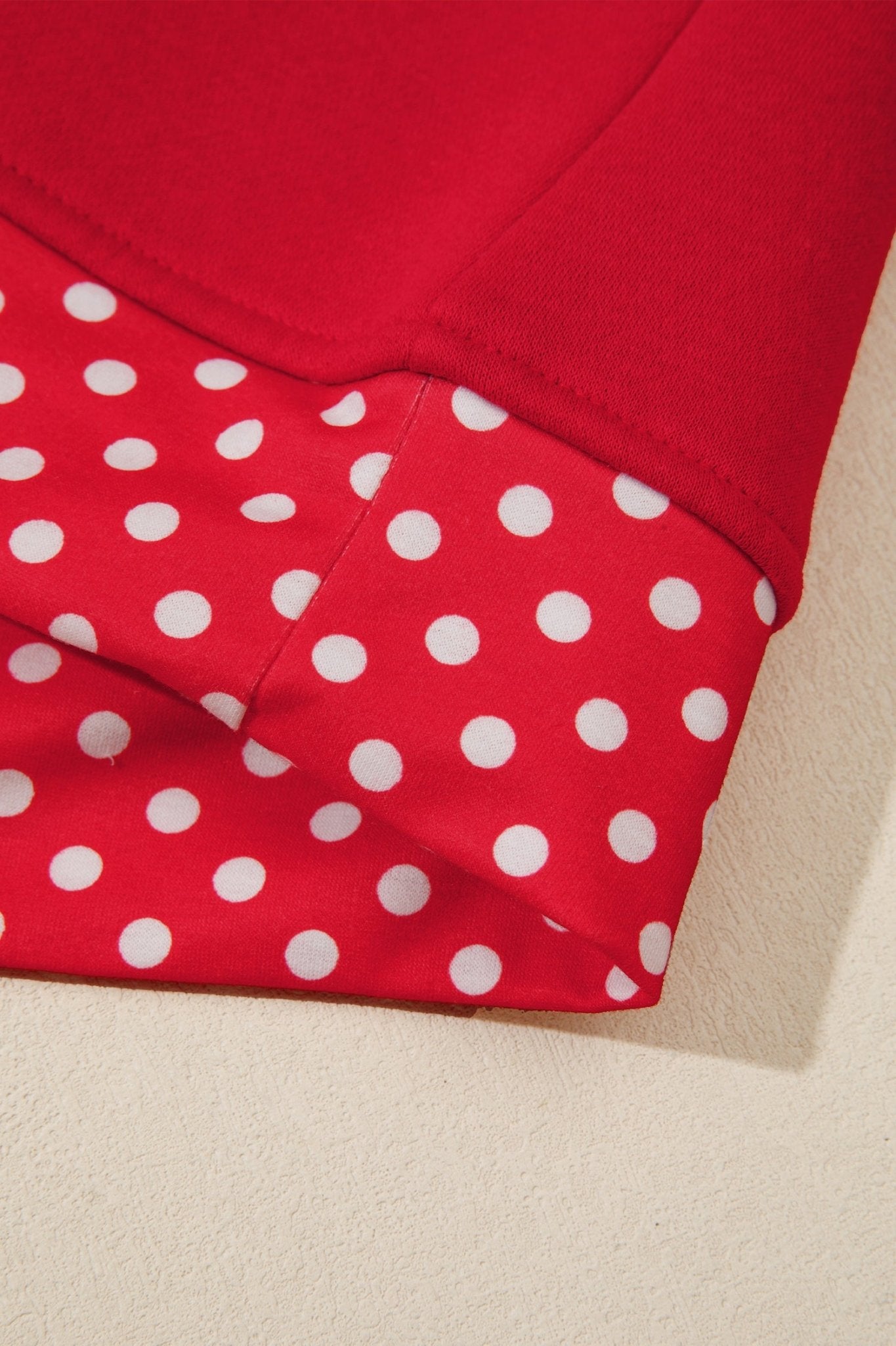 Close-up of folded red garment with white polka-dot section and solid red fabric on light beige.