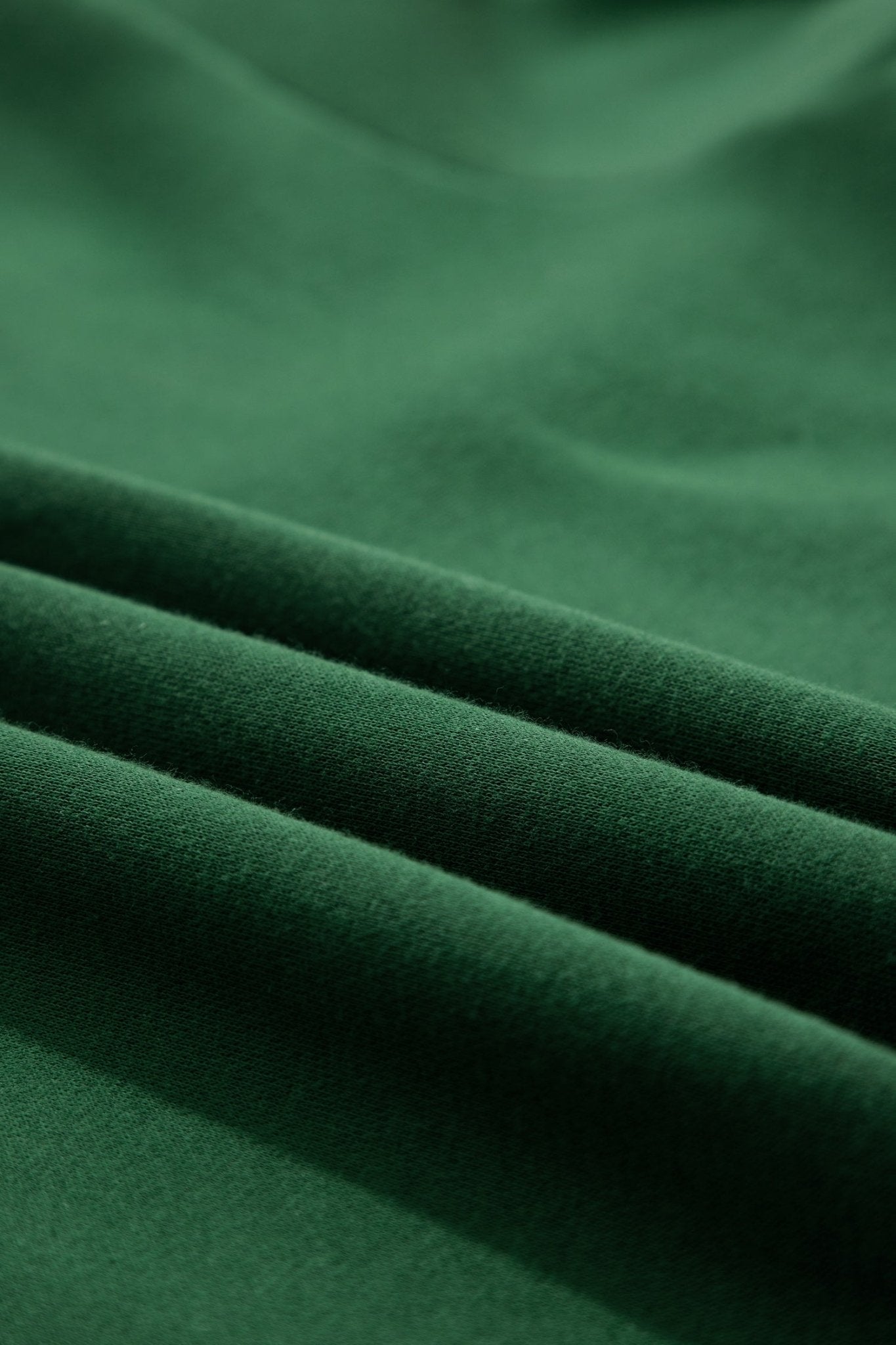 A close-up of dark forest green fabric with soft folds and a smooth texture.