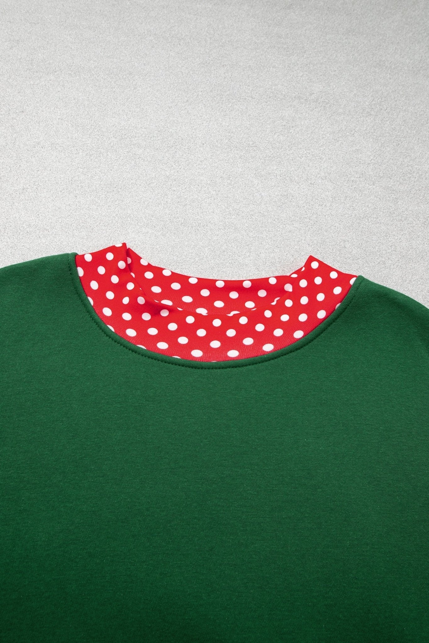 Close-up of green crewneck garment with red inner collar featuring white polka dots on light gray.