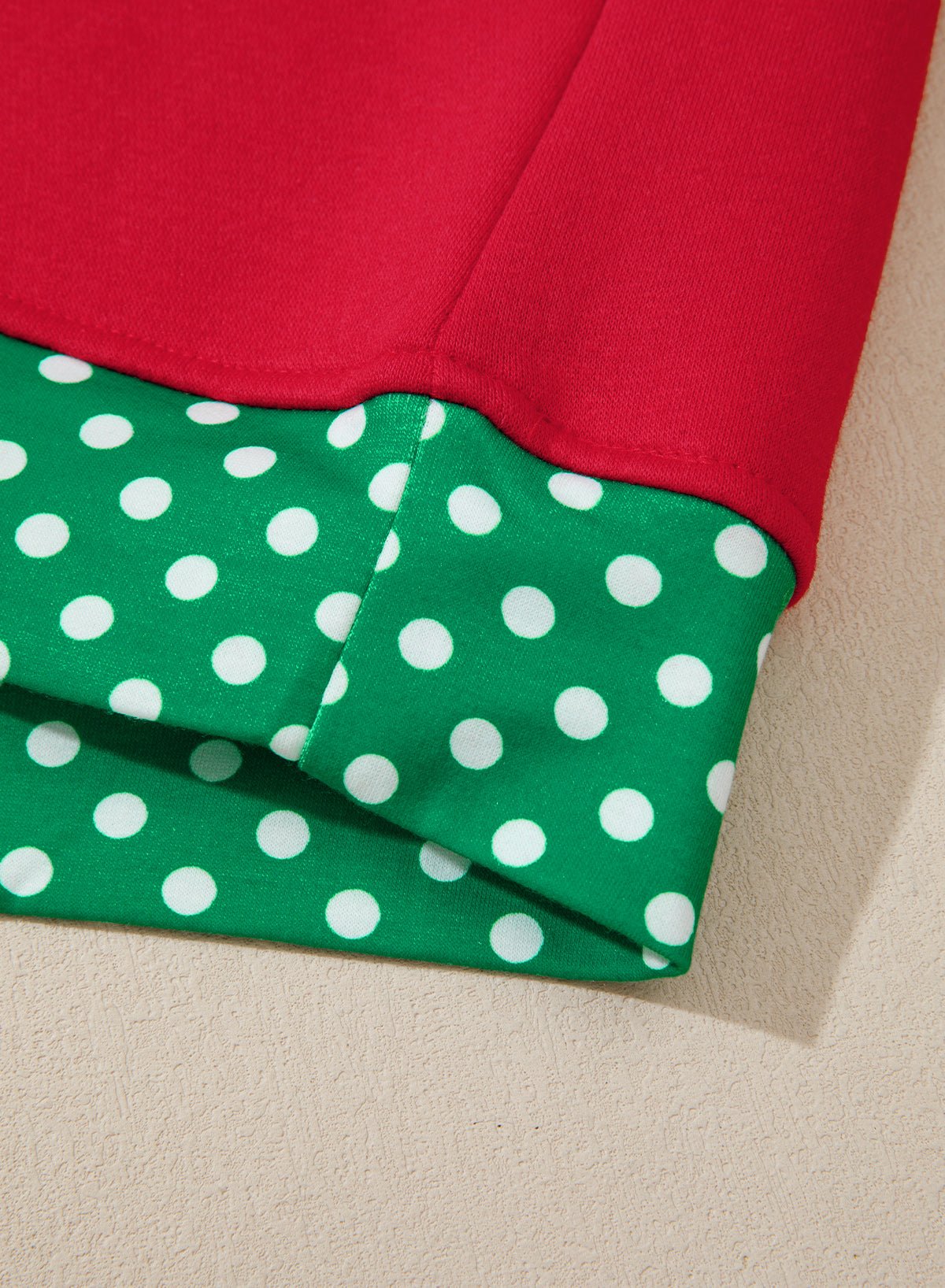 Close-up of red garment with contrasting green-white polka-dot inner collar on a beige background.