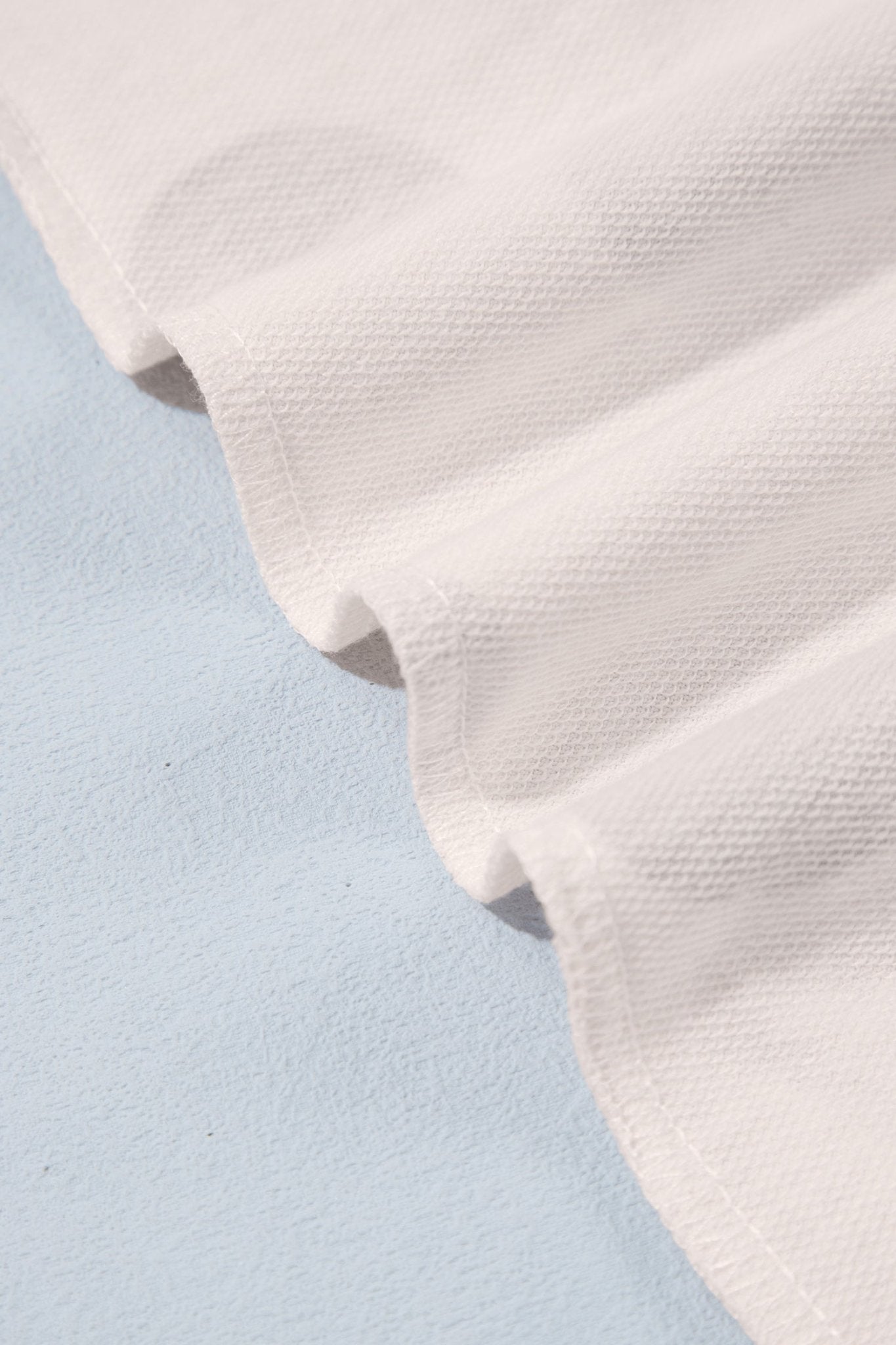 Close-up of textured off-white cotton or linen fabric draped on light blue surface.