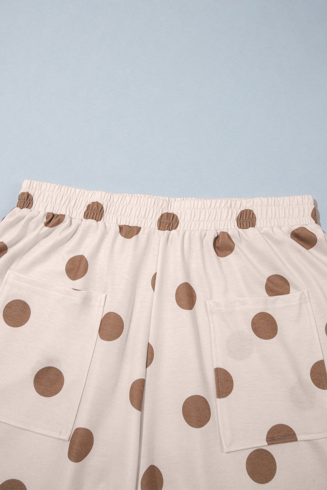 Close-up of cream polka dot shorts with elastic waist and front patch pockets on blue.