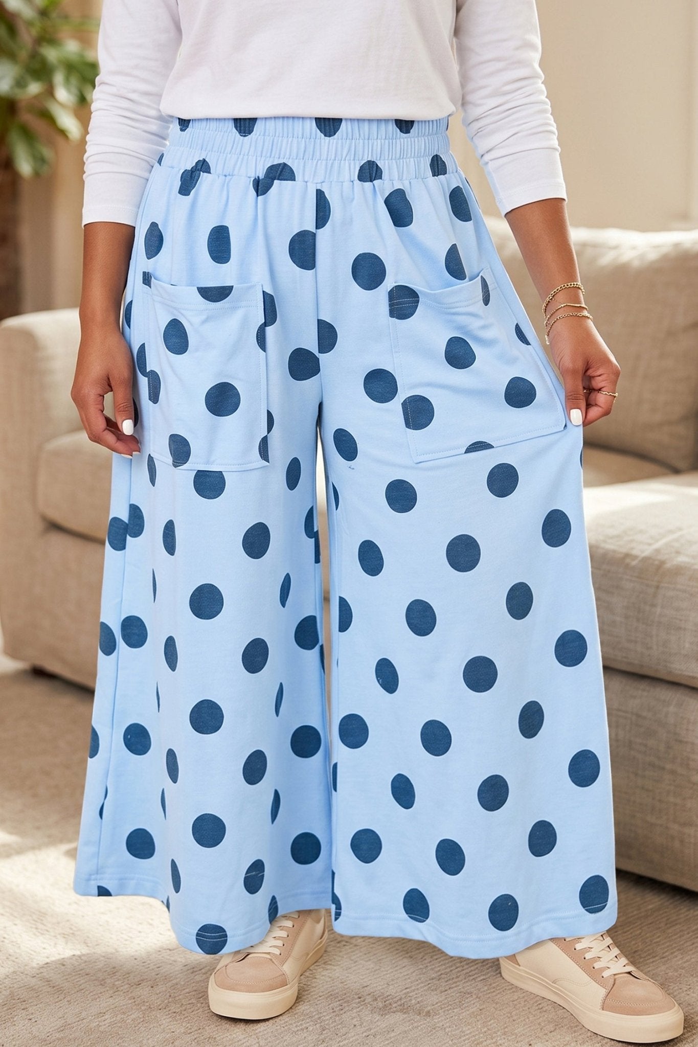 Person wearing light blue wide-leg polka-dot pants, white long-sleeve top, and beige sneakers indoors.