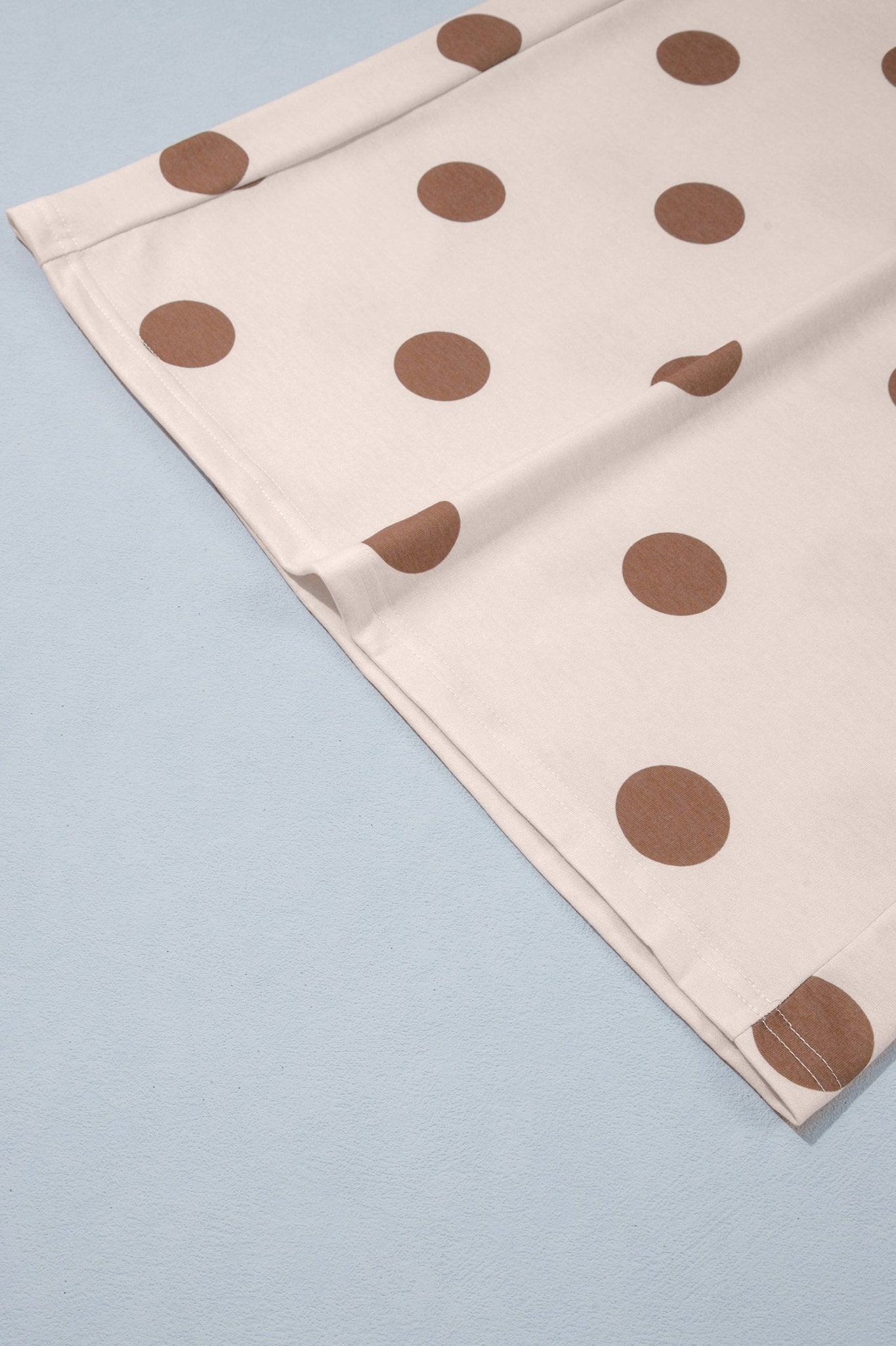 Close-up of light beige brown polka dot fabric laid diagonally on a light blue surface.