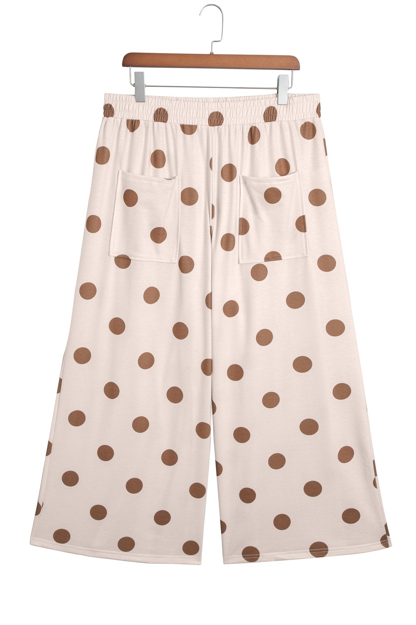 Wide-leg cropped light cream pants with brown polka dots on a wooden hanger against white.