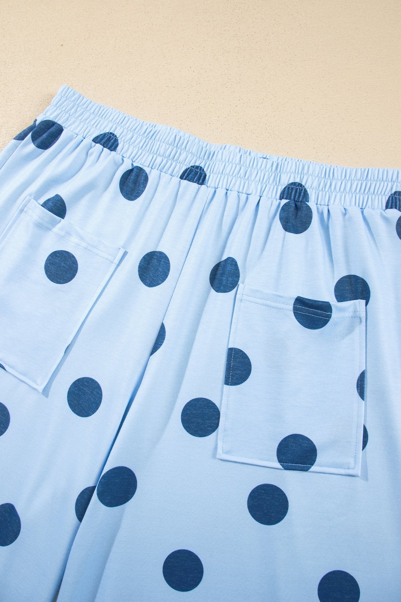 Light blue pajama pants with dark blue polka dots, elastic waistband, and front patch pocket on beige.