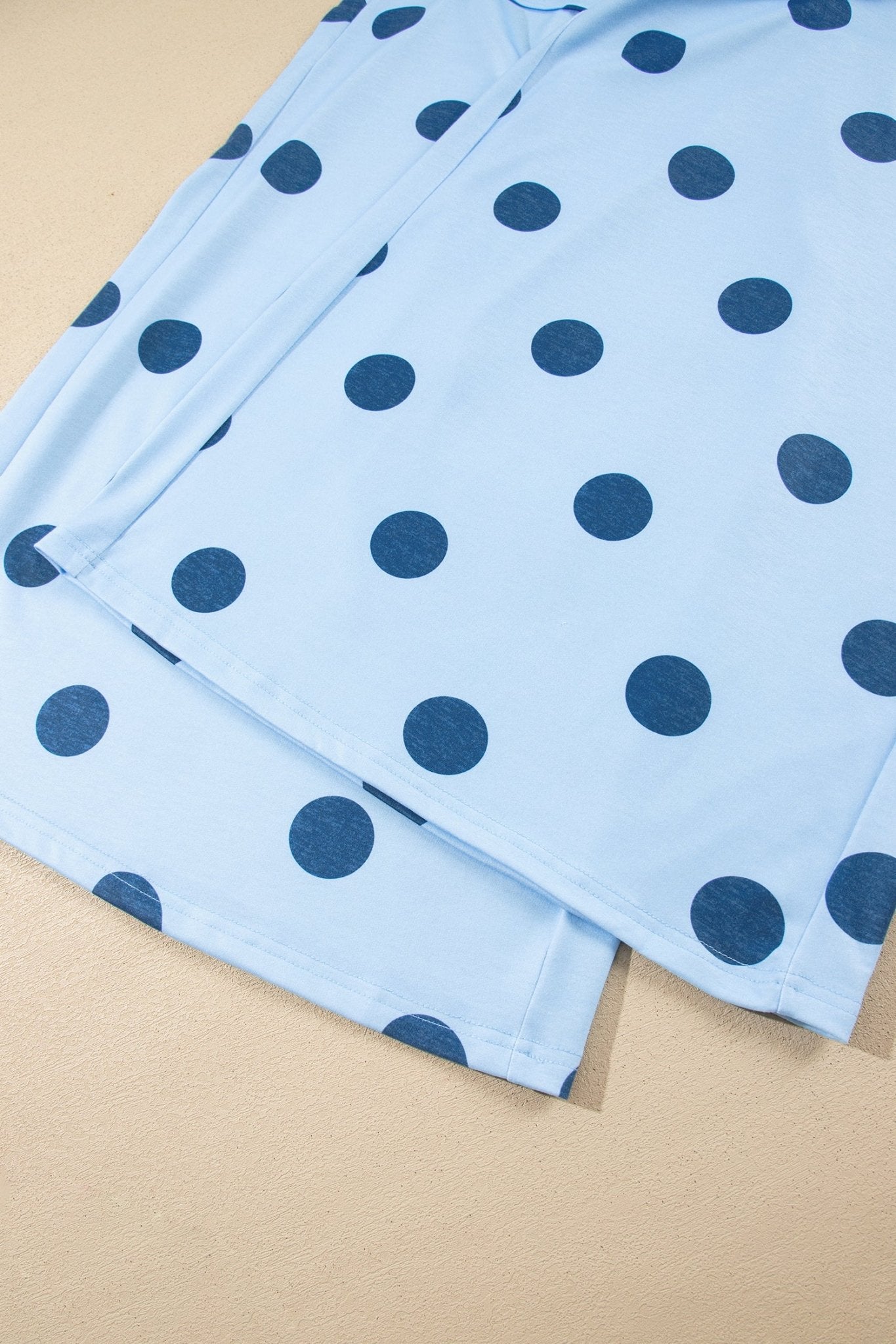 Light blue pajama pants with a dark blue polka dot pattern, folded on a beige textured surface.