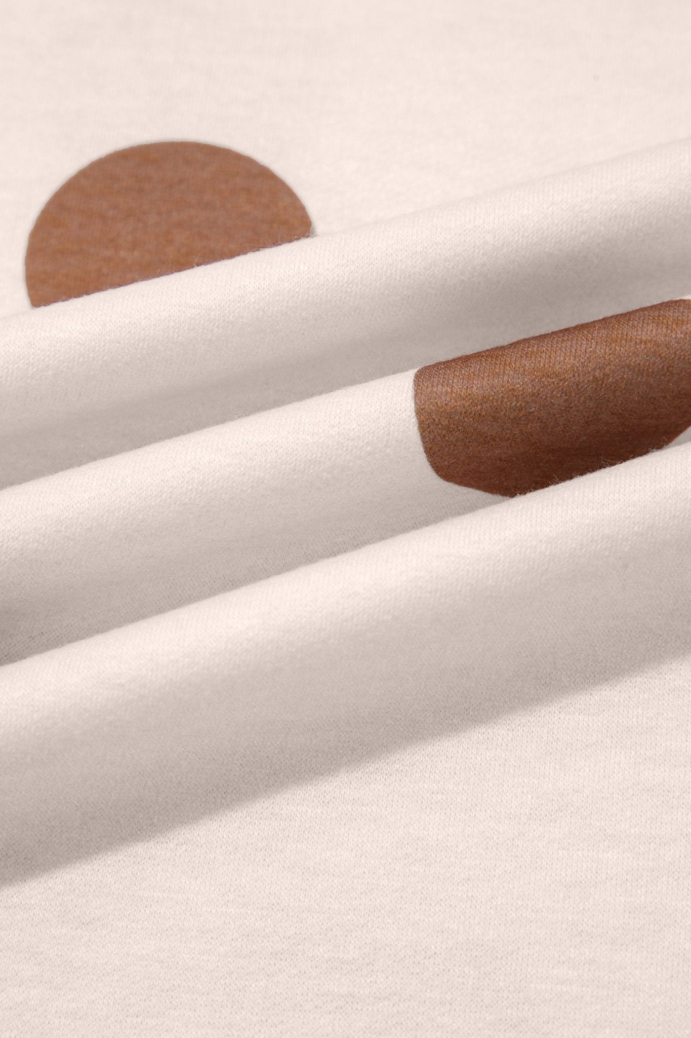 Close-up of cream fabric with brown circular and rectangular graphics showing material folds and texture.