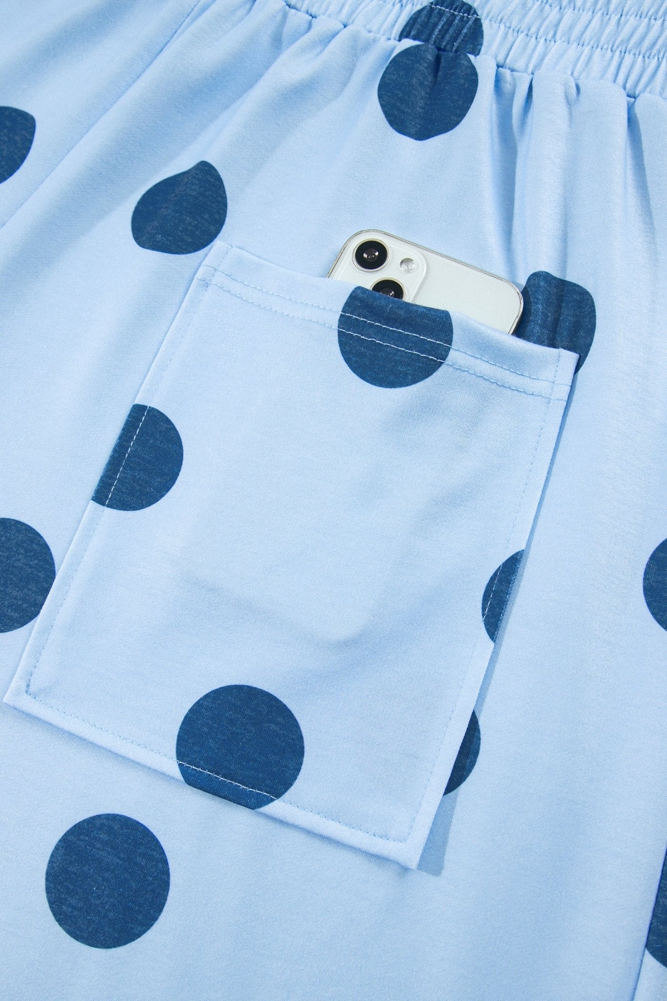 Close-up of light blue polka-dot garment with front pocket holding a white smartphone.